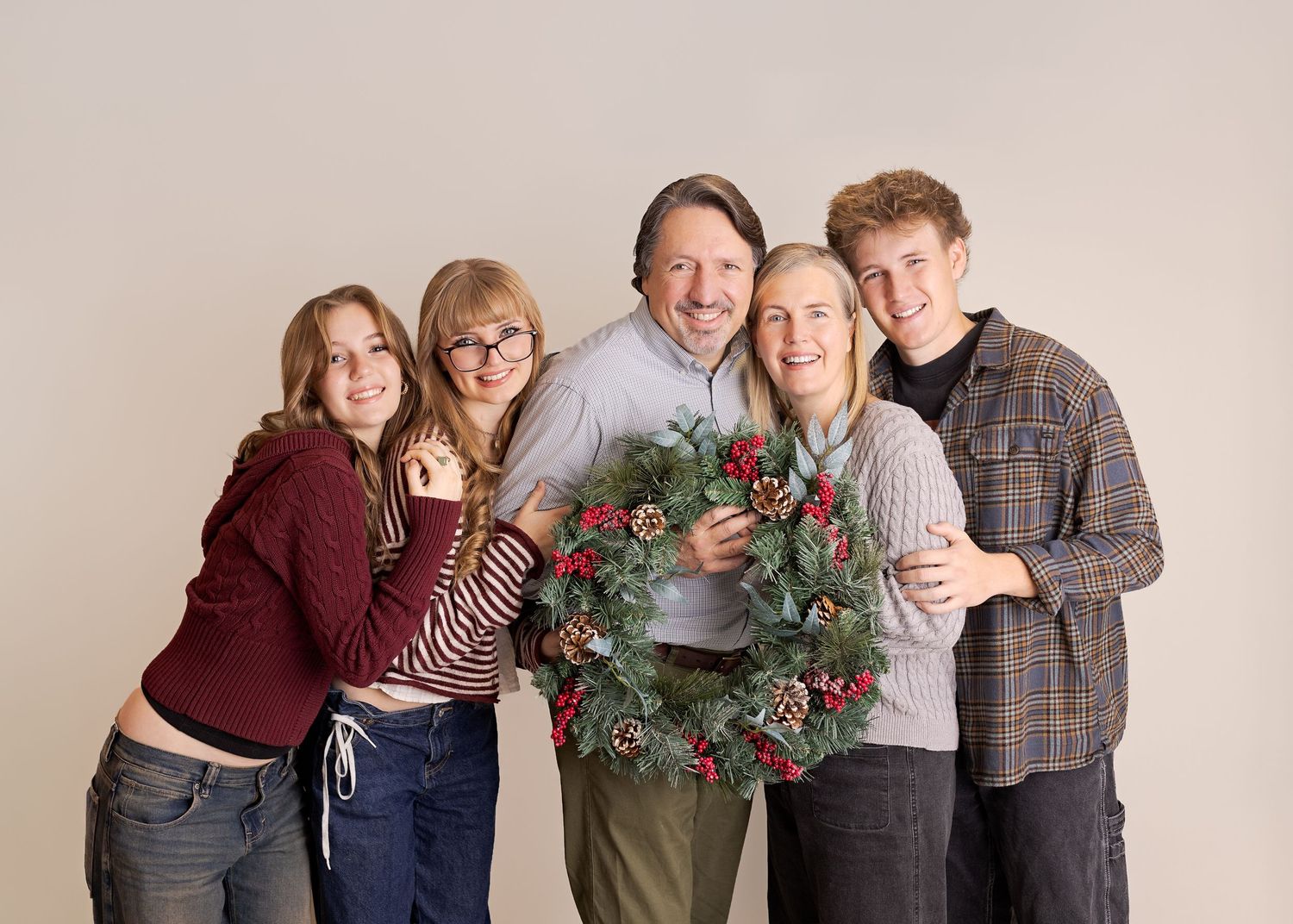 Five people wearing casual clothing pose together against a gray backdrop in a studio setting.