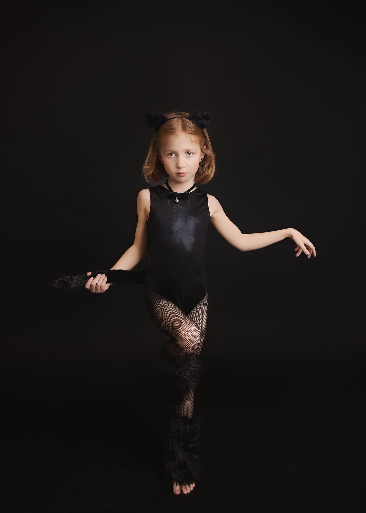 Dancer wearing black leotard strikes elegant pose against dark background.