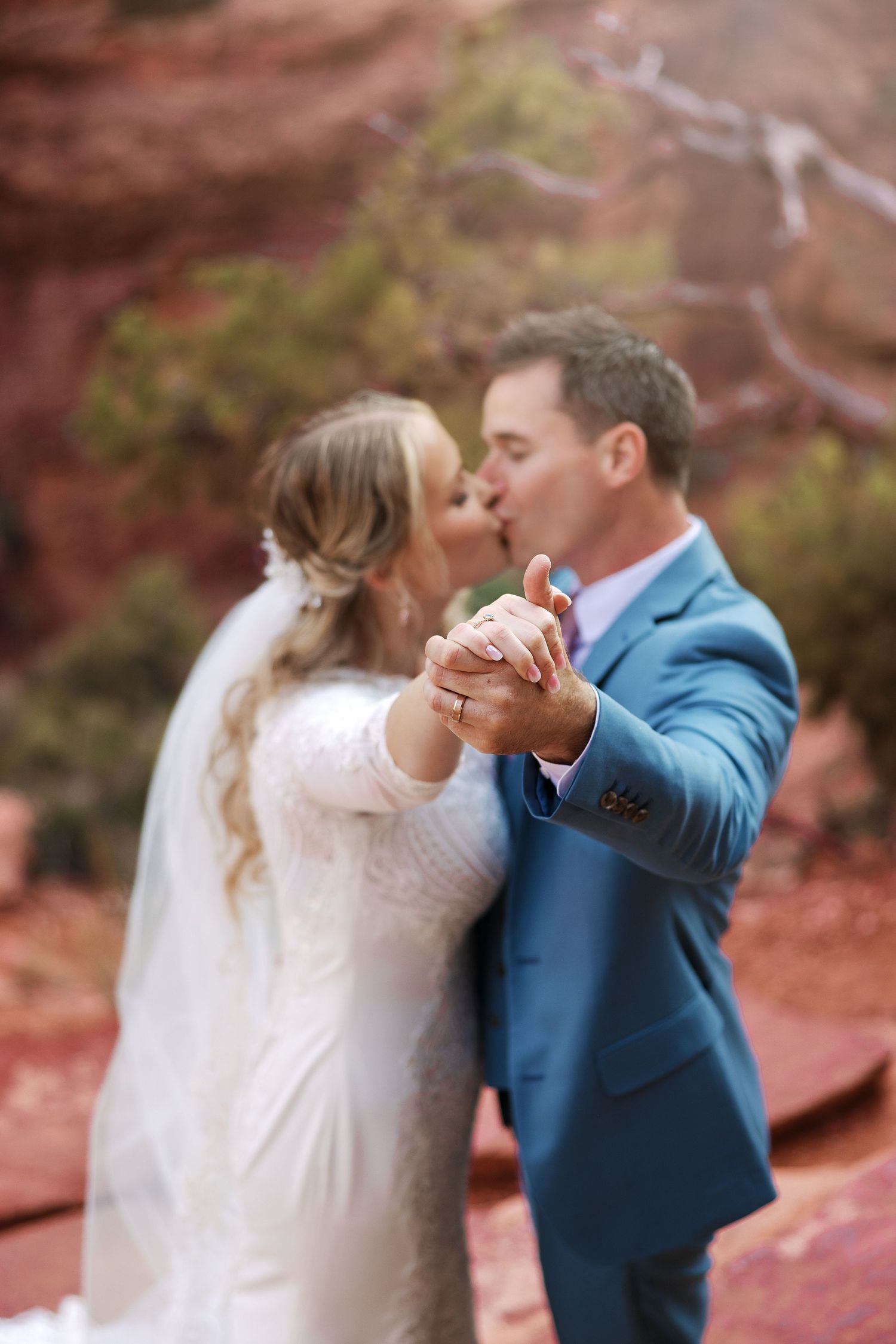 Two people in wedding attire sharing a romantic dance outdoors with autumn foliage in the background.