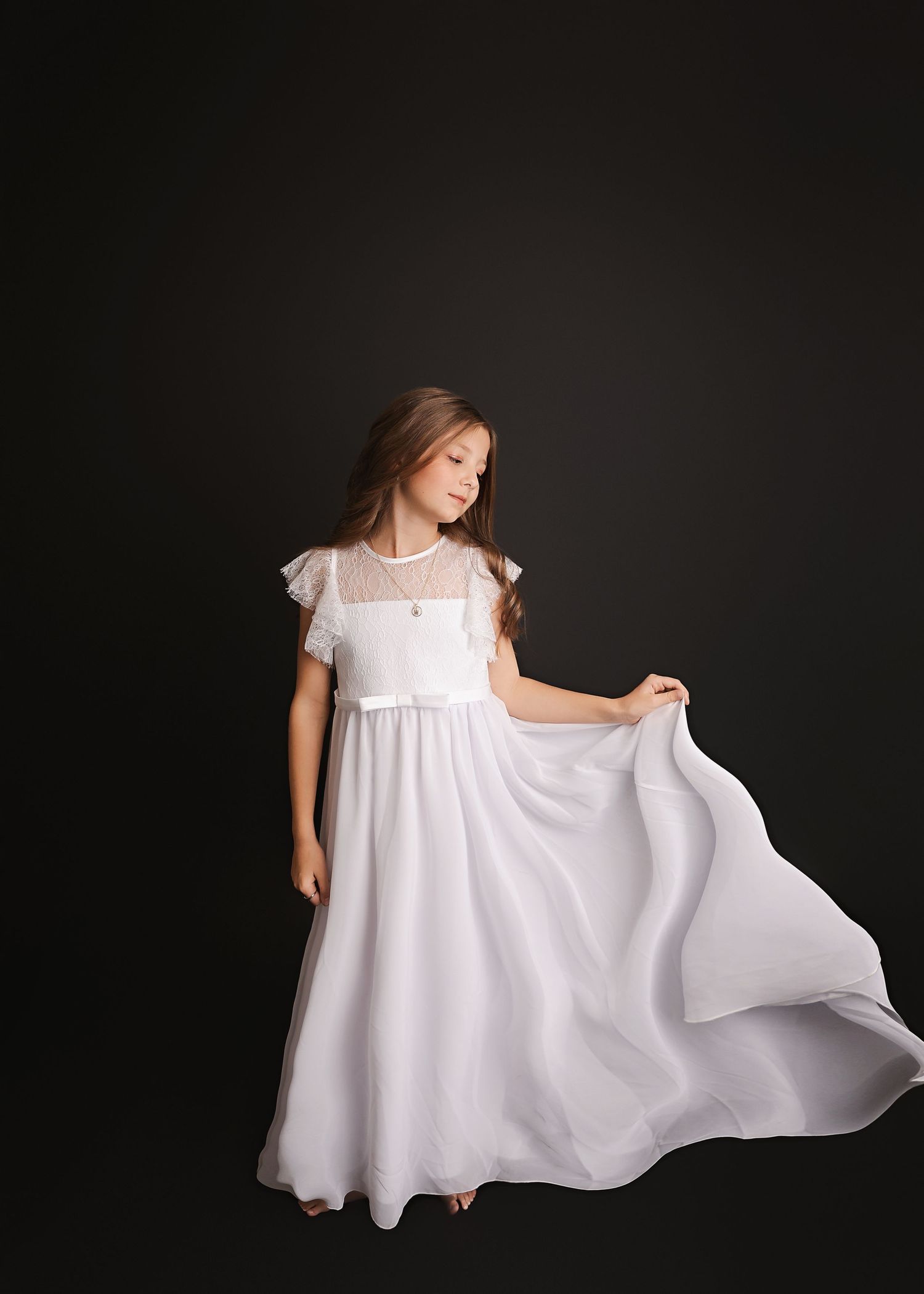A flowing white dress twirls elegantly against a dark studio backdrop.