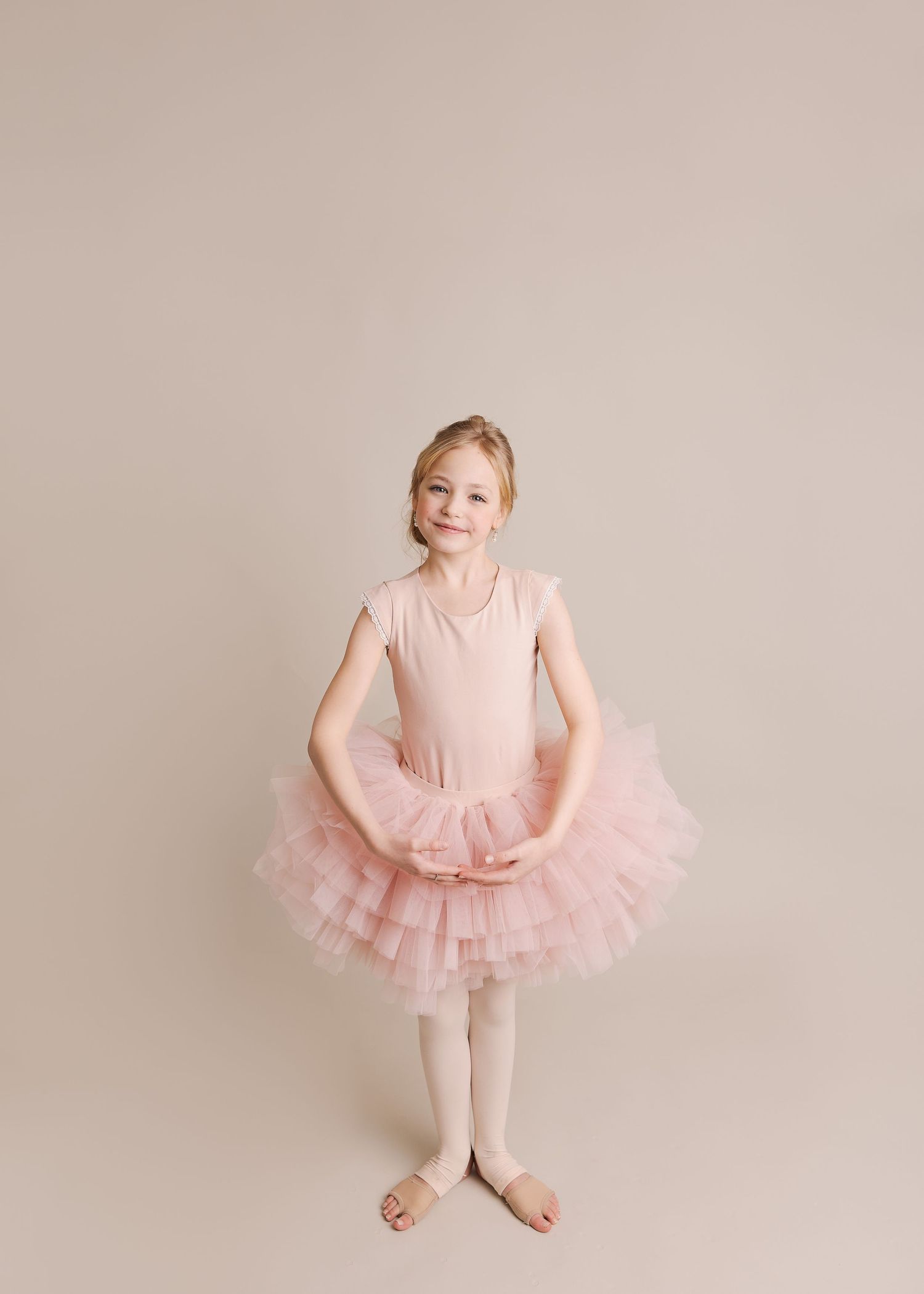 Young ballet dancer in pink tutu standing gracefully against neutral backdrop.