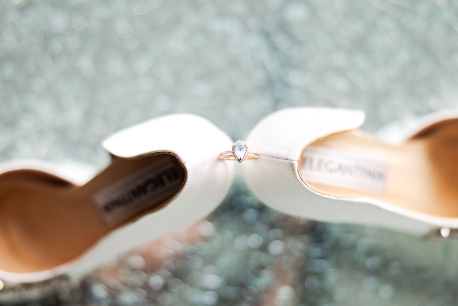 Two white wedding pumps holding a wedding ring in close-up view with blurred background.