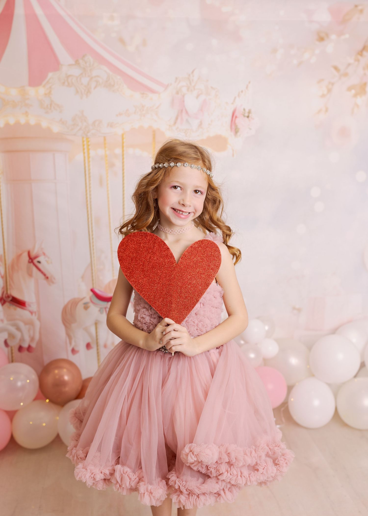 Sweet Valentine's Day photo session with pink tulle dress and red heart prop in a dreamy pastel setting.