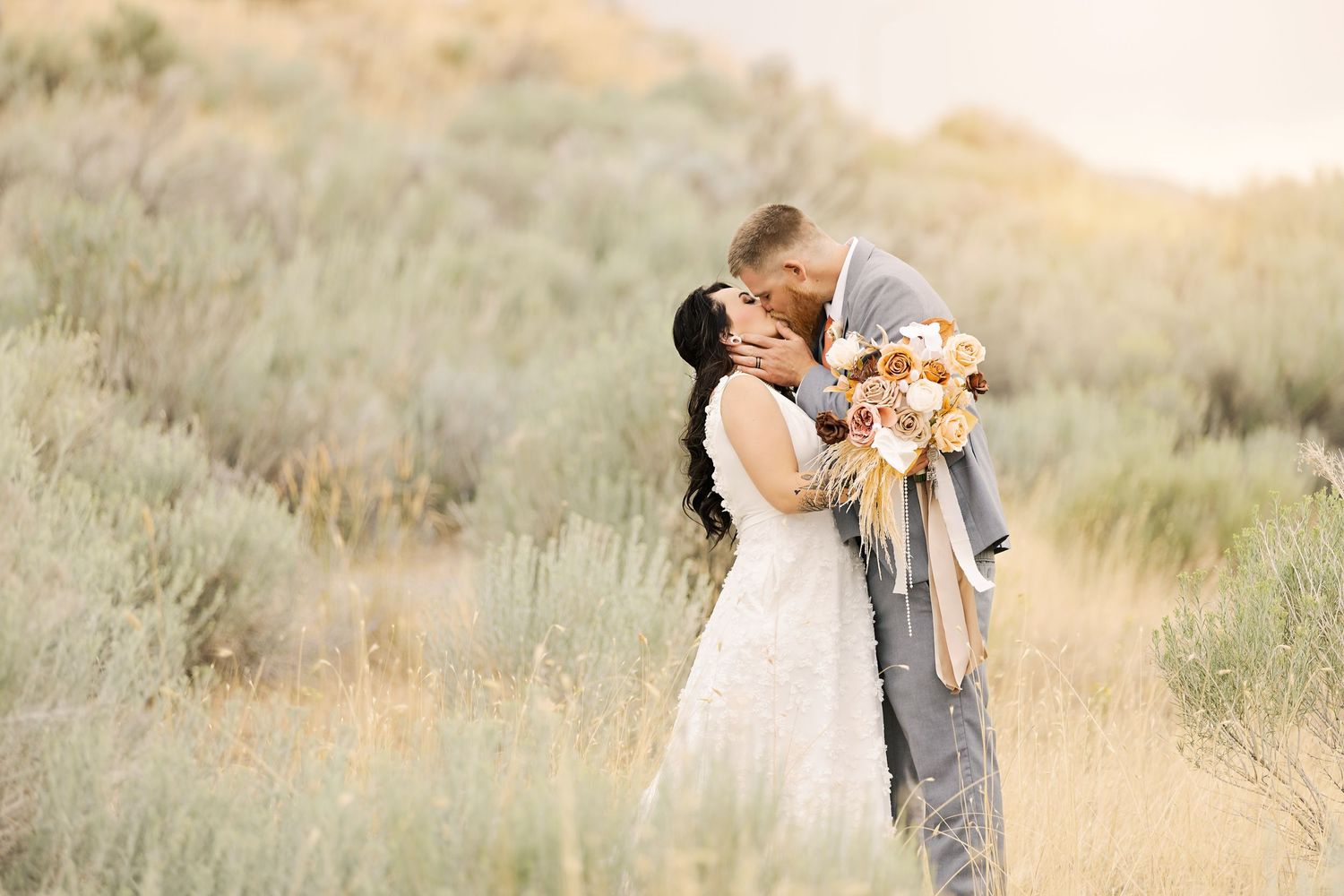 Intimate wedding moment captured in golden light among desert brush with autumn-toned bouquet.