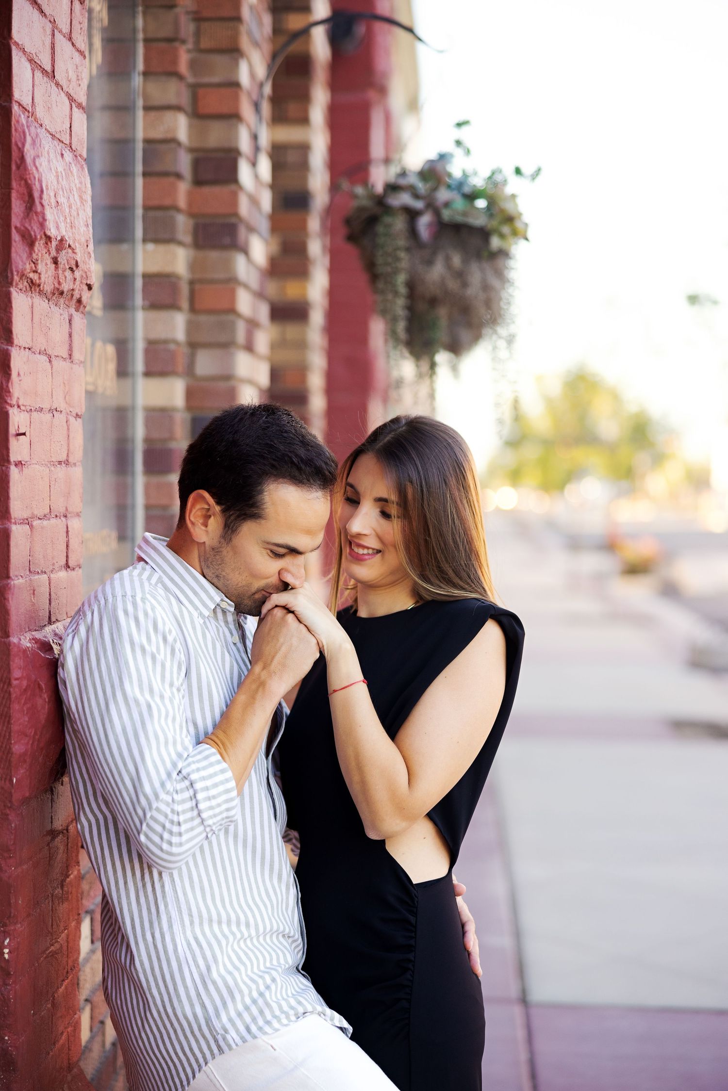 Couple shares intimate moment against brick wall with hanging flowers.