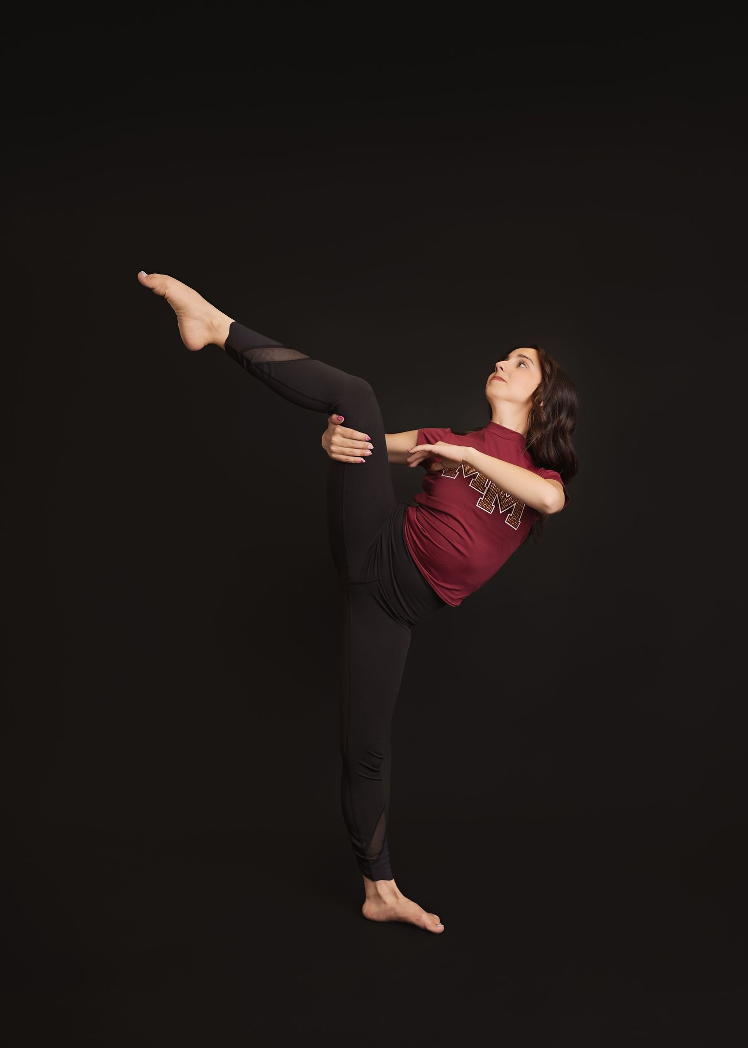 Dancer performs expressive modern dance movements against dark background in burgundy top and black pants.