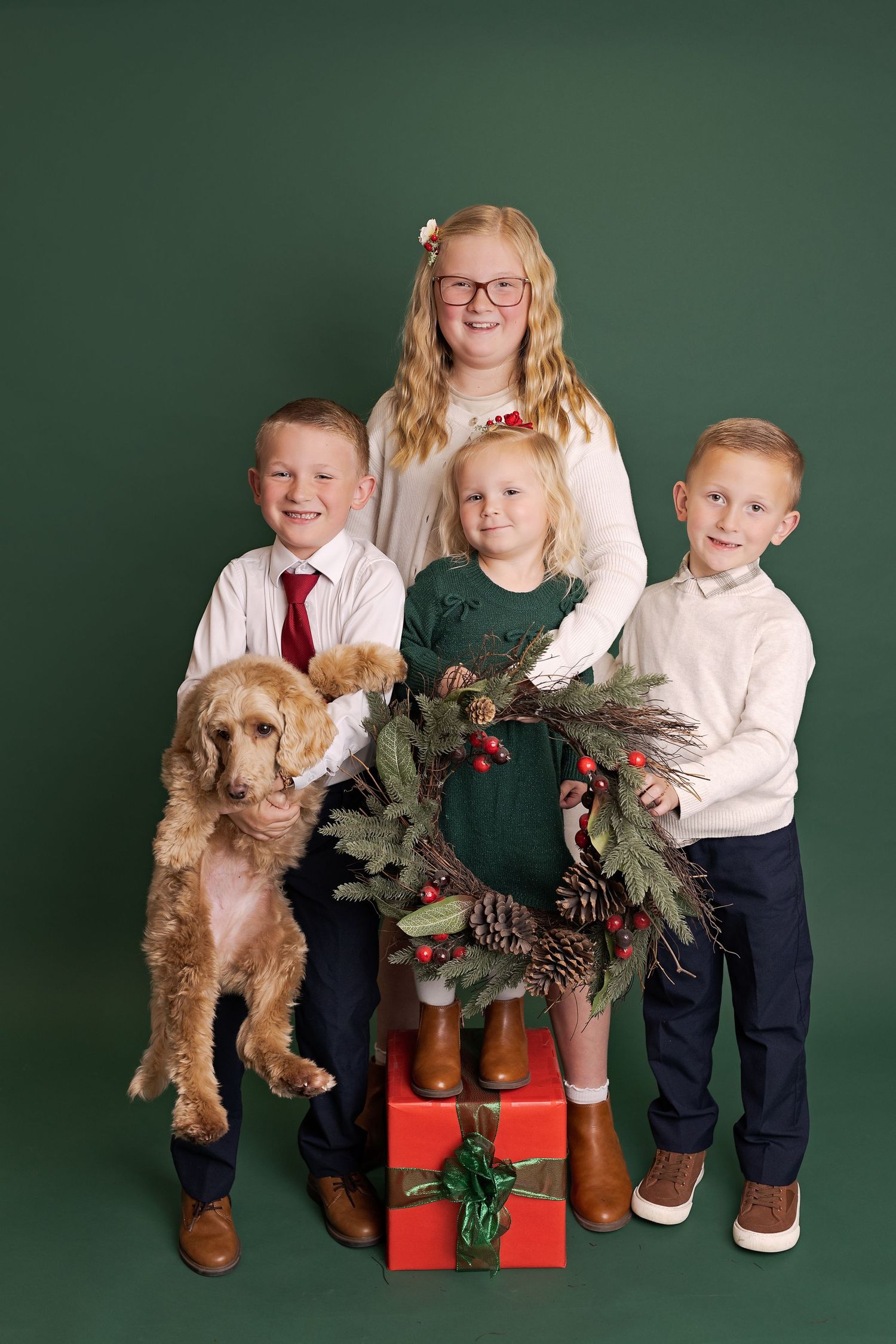 Holiday family portrait series with children in matching white sweaters and a small dog against a dark green backdrop.