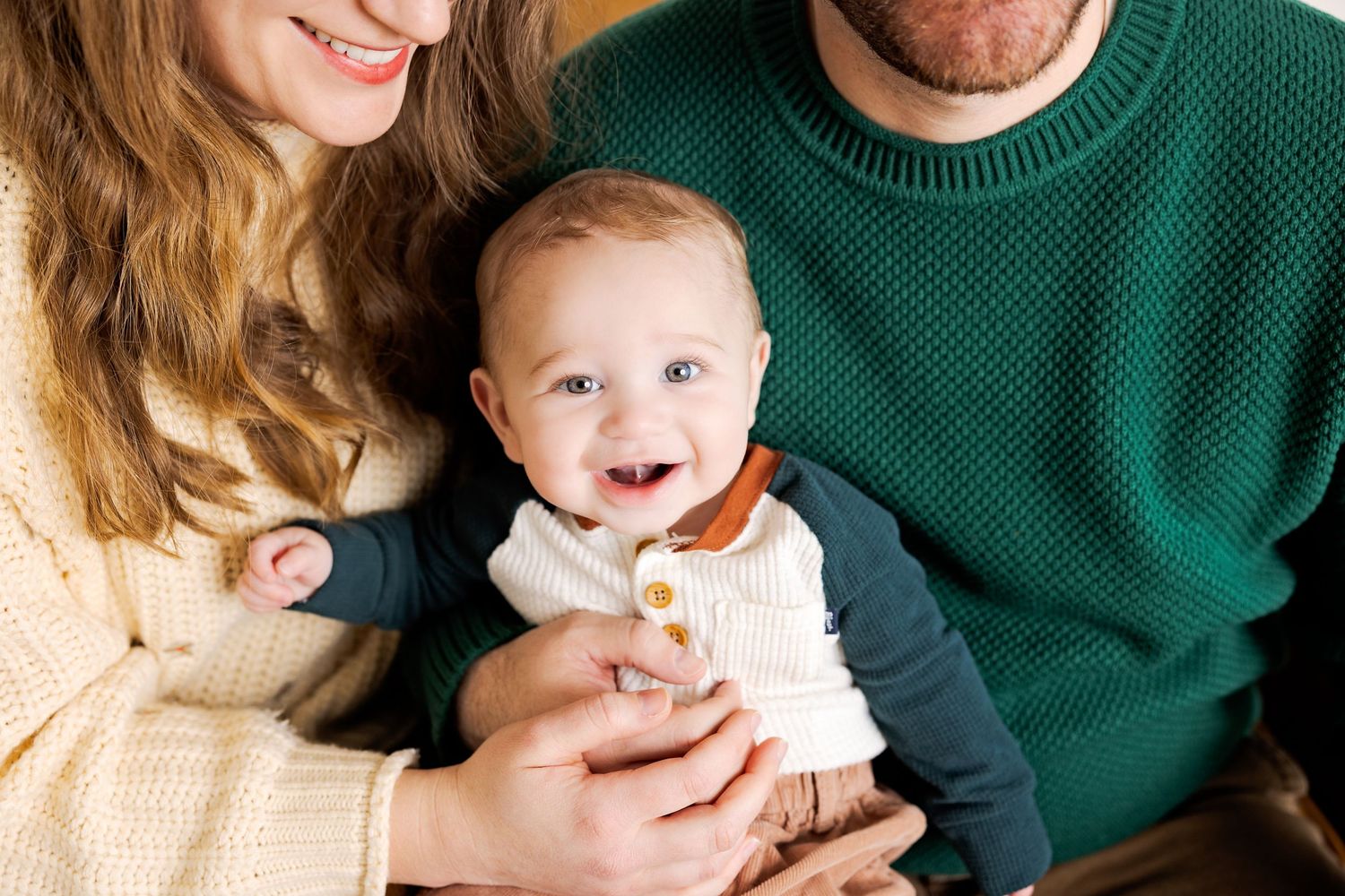 A joyful family wearing cozy sweaters laughs together while sitting on a cream-colored couch.