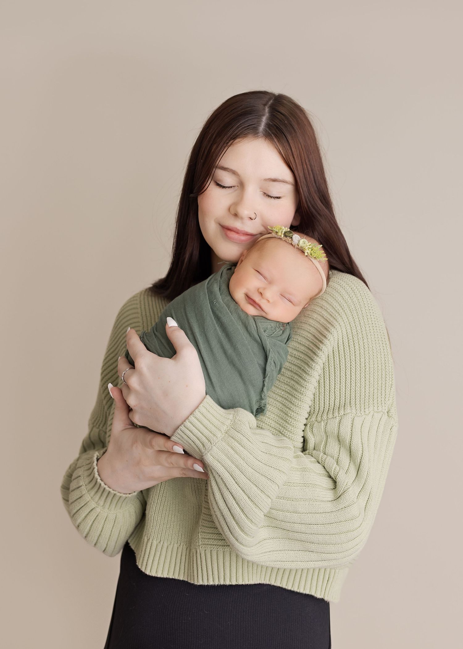A tender moment between mother and newborn wearing sage green during a minimalist studio portrait session.