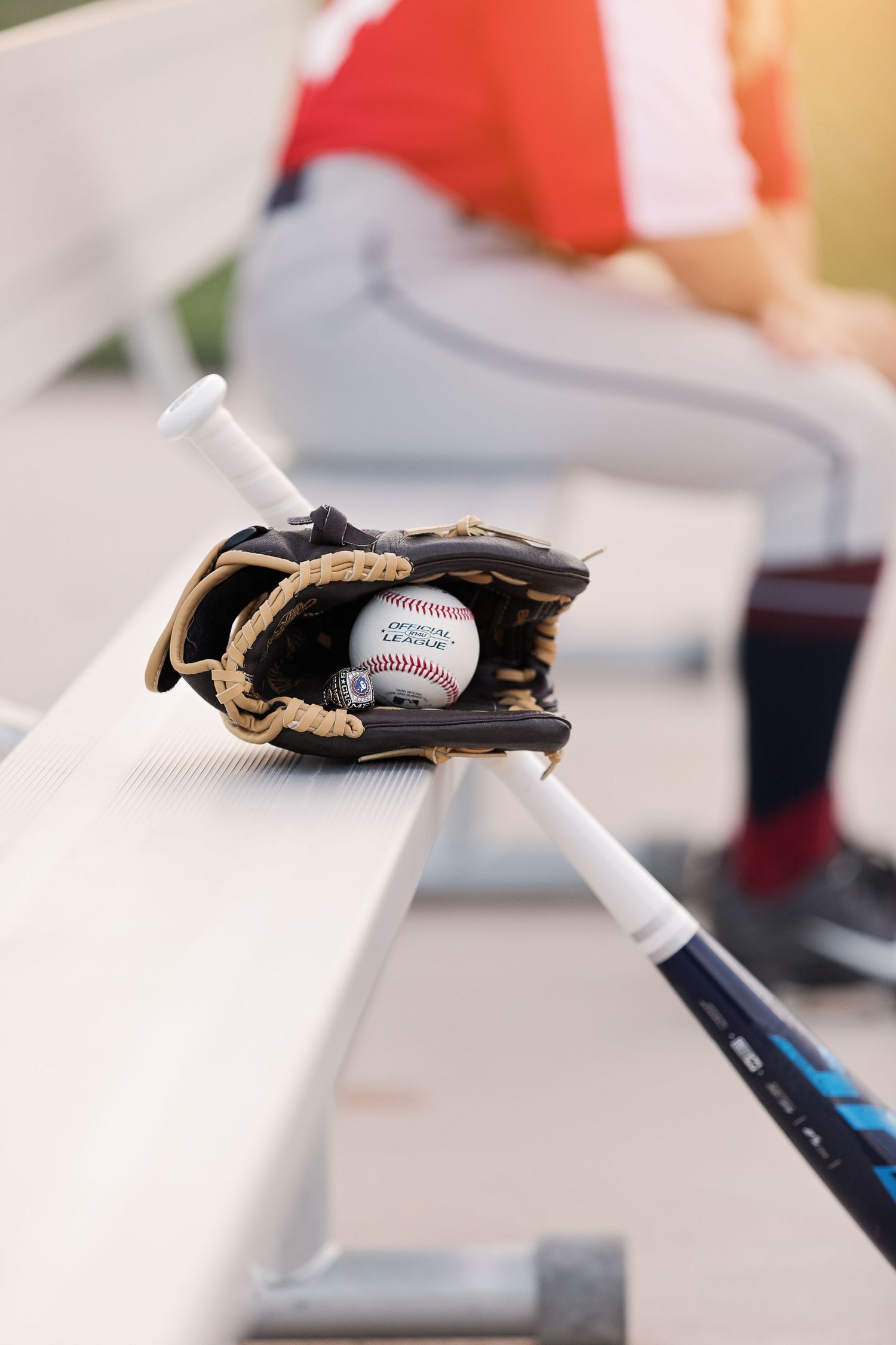 Baseball glove and ball resting on dugout bench with player in background.