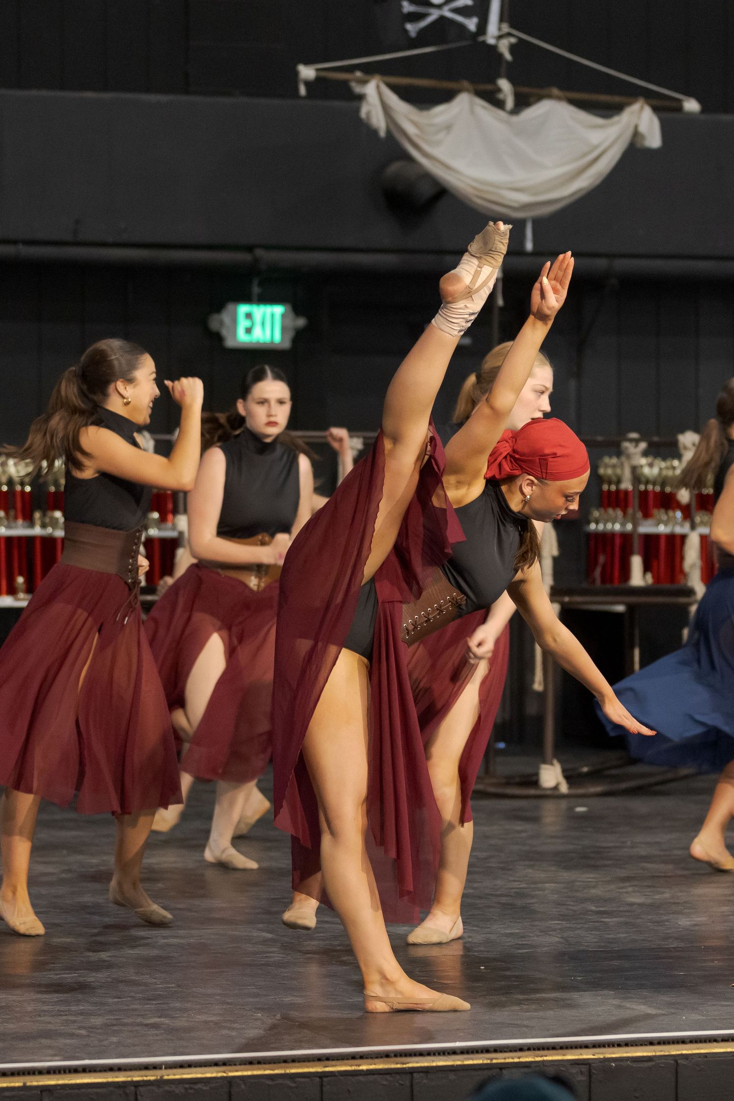 Dancers perform an expressive contemporary dance routine on stage wearing burgundy costumes and flowing skirts.