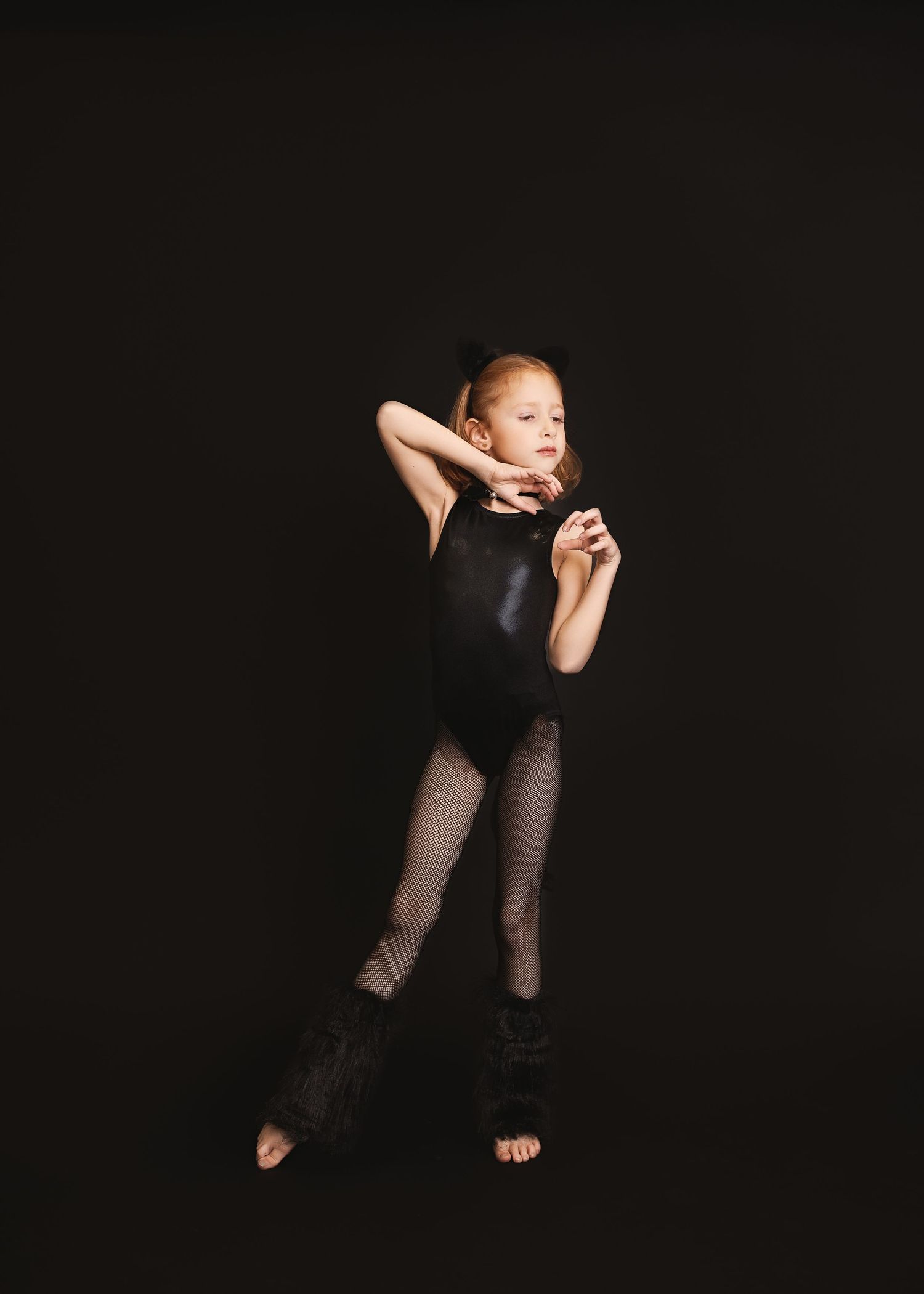 A dancer in black attire stretches gracefully in a dramatic low-light pose against a dark background.