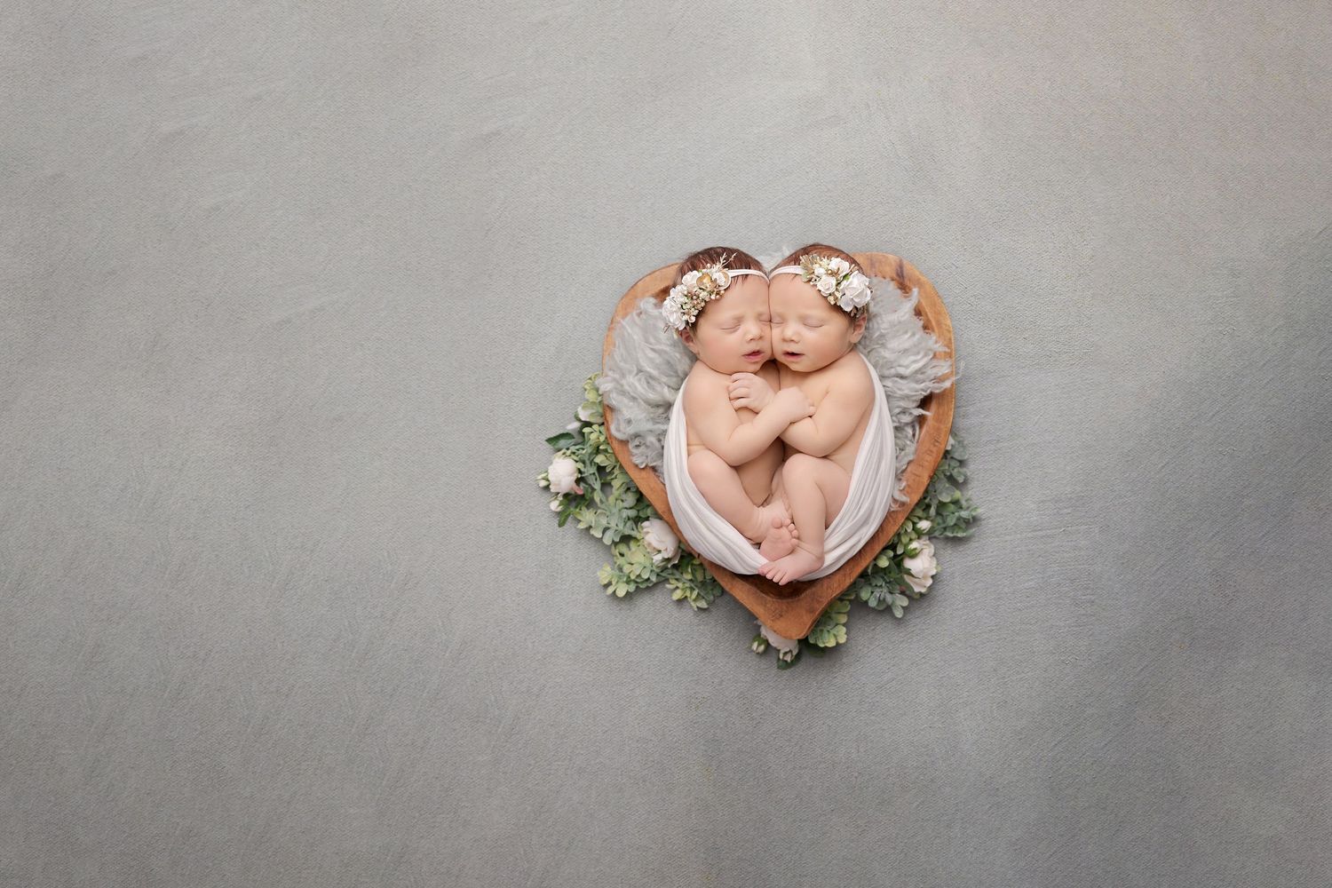 An artistic overhead newborn photo in a heart-shaped basket with botanical accents.