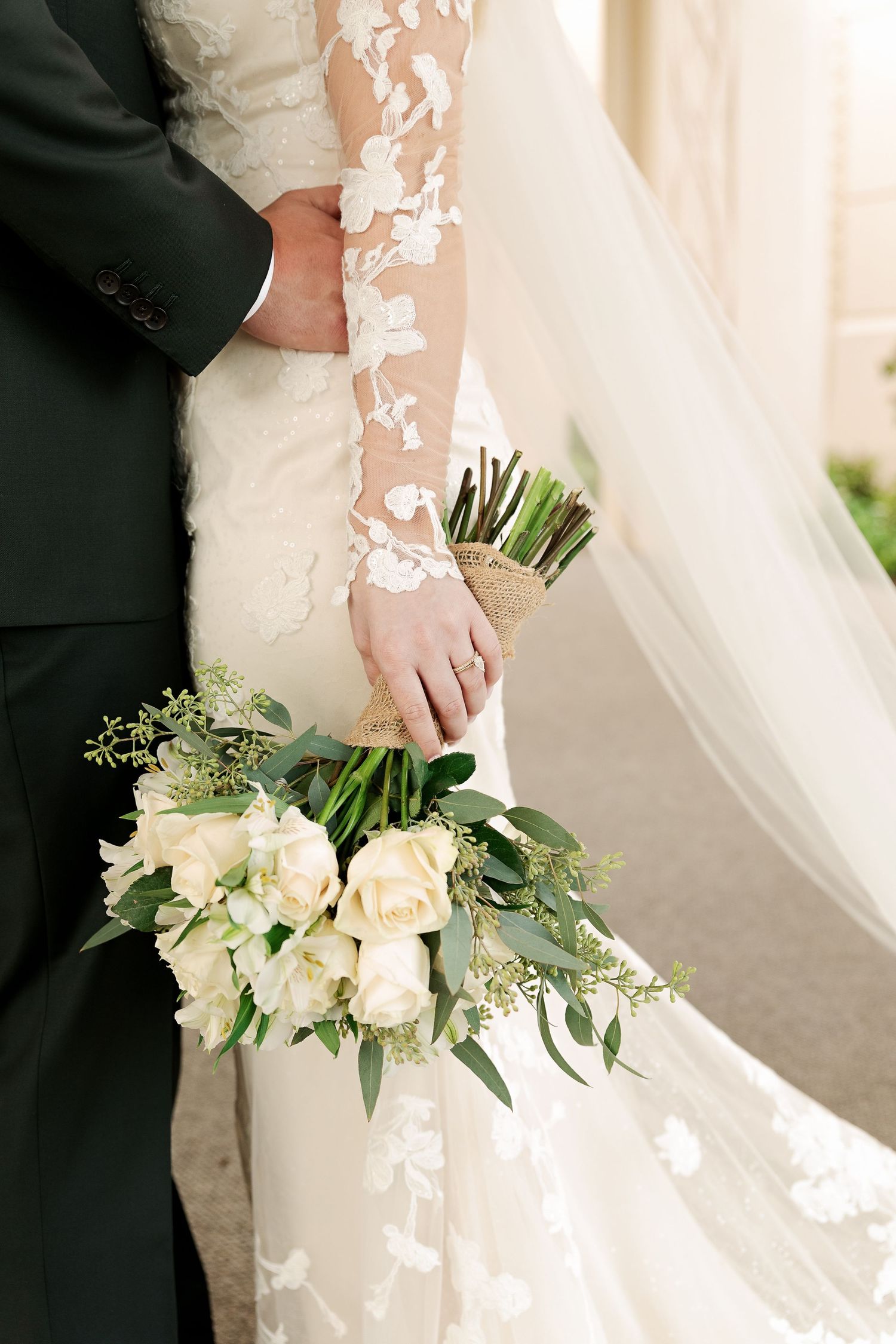 Close up of bride's bouquet with white roses and greenery against lace dress.