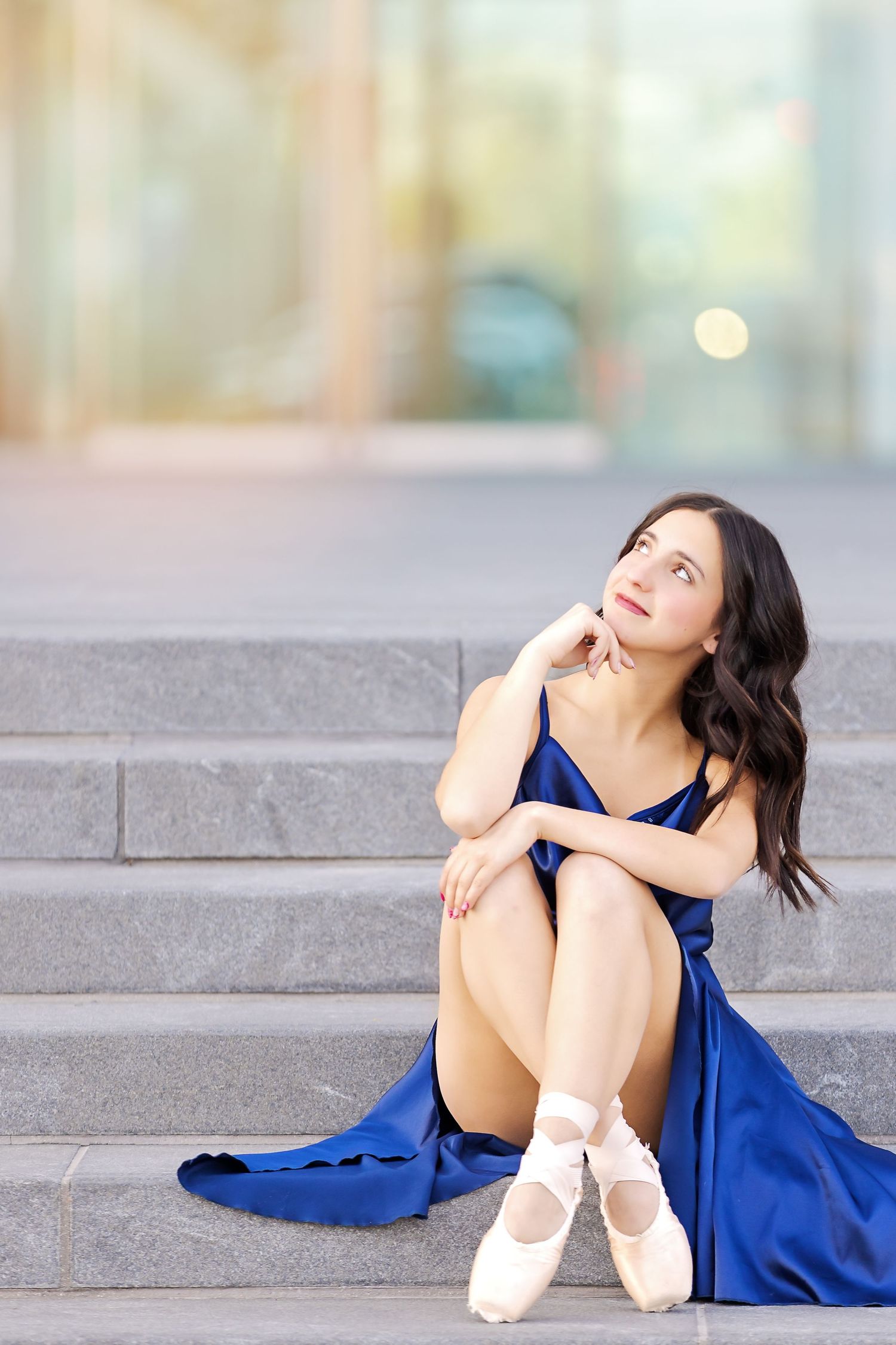 A dancer in a flowing royal blue dress poses gracefully on stone steps while wearing ballet pointe shoes.