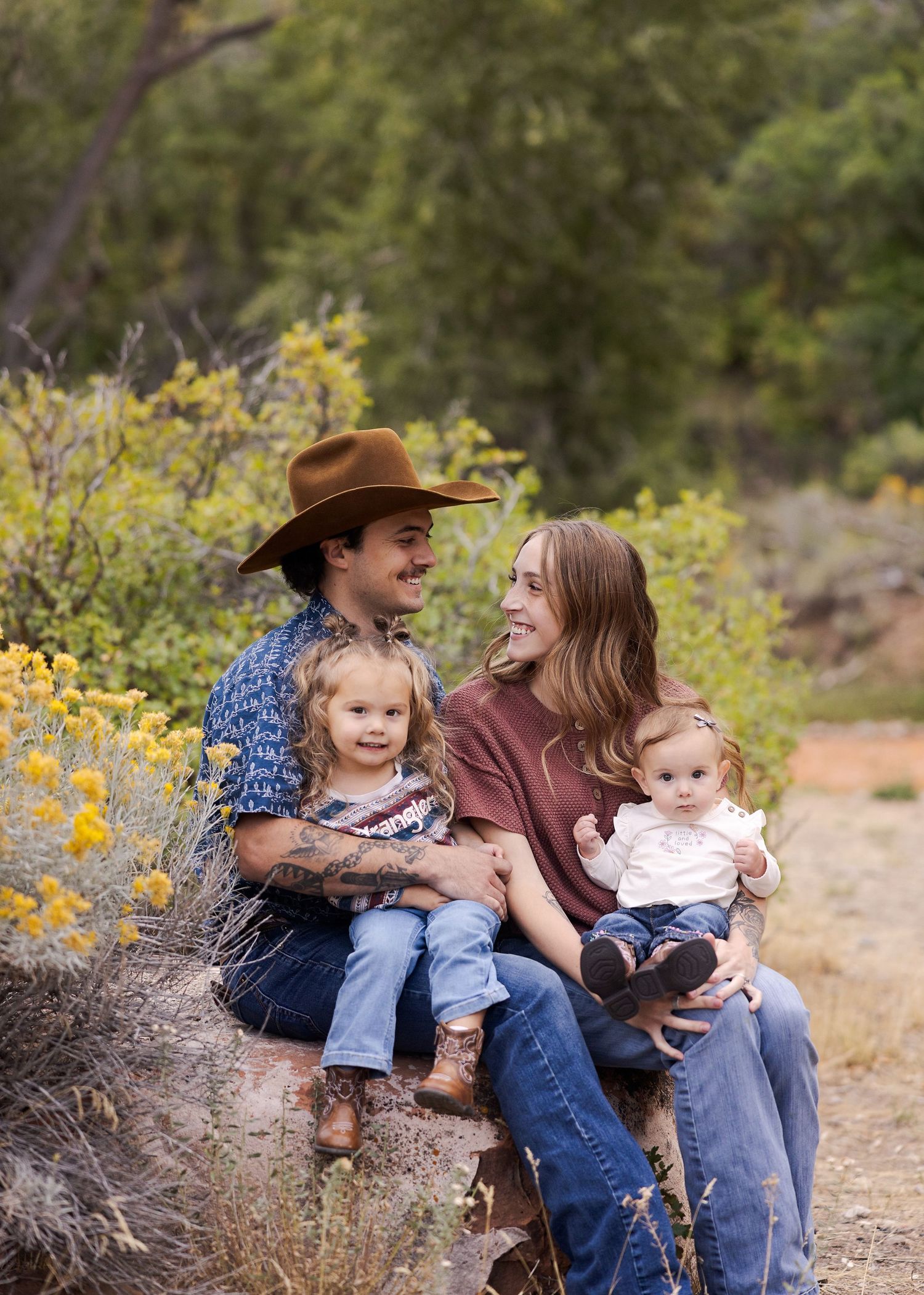 Young family with two toddlers sitting on a log surrounded by yellow wildflowers in a desert landscape.