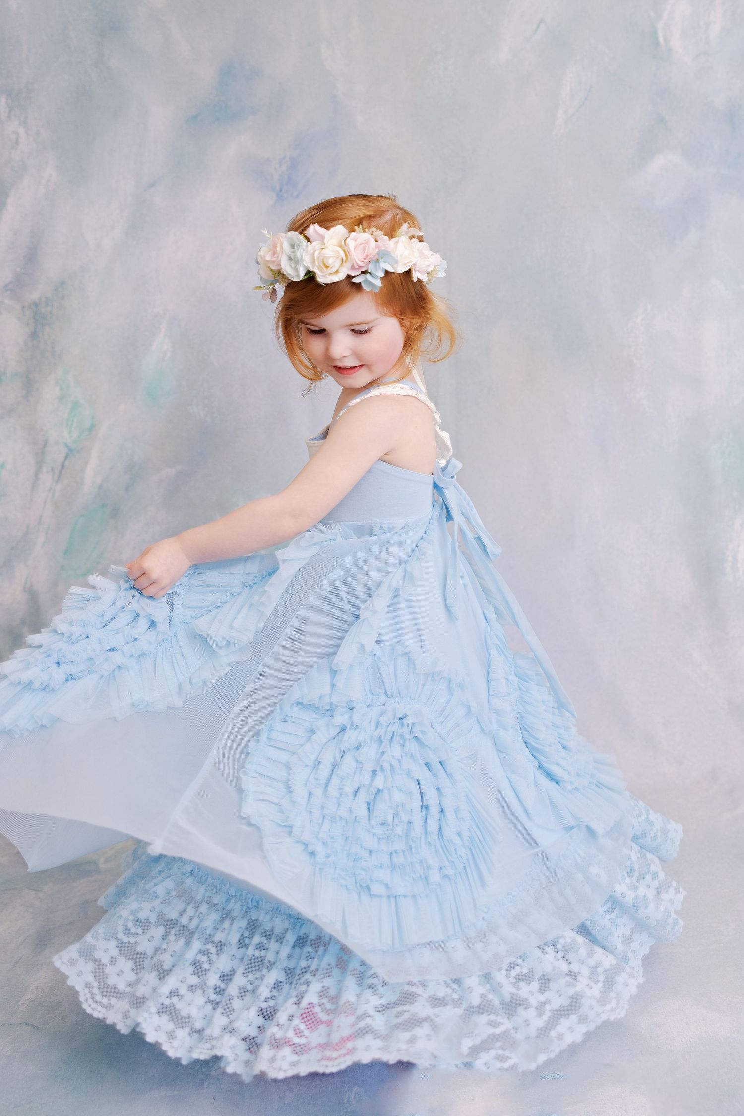 Twirling portrait in flowing blue lace dress with floral crown and dreamy background.