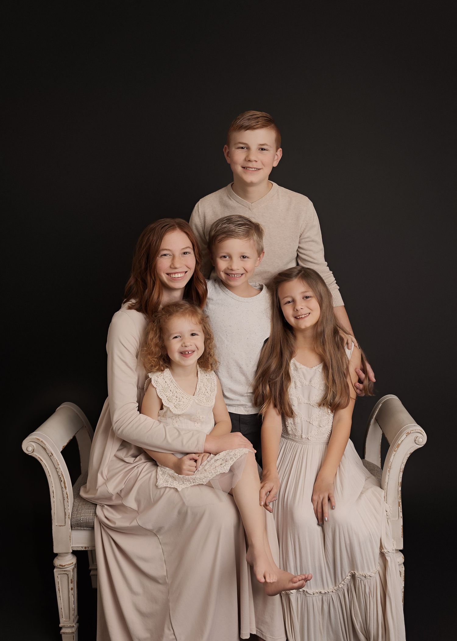 Family portrait on an antique chair wearing neutral colors against a dark backdrop.