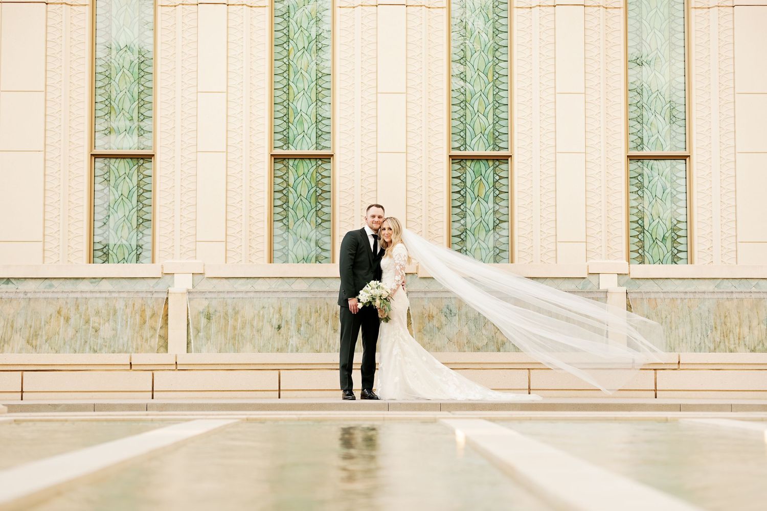 Wedding couple standing outside temple with long flowing veil.