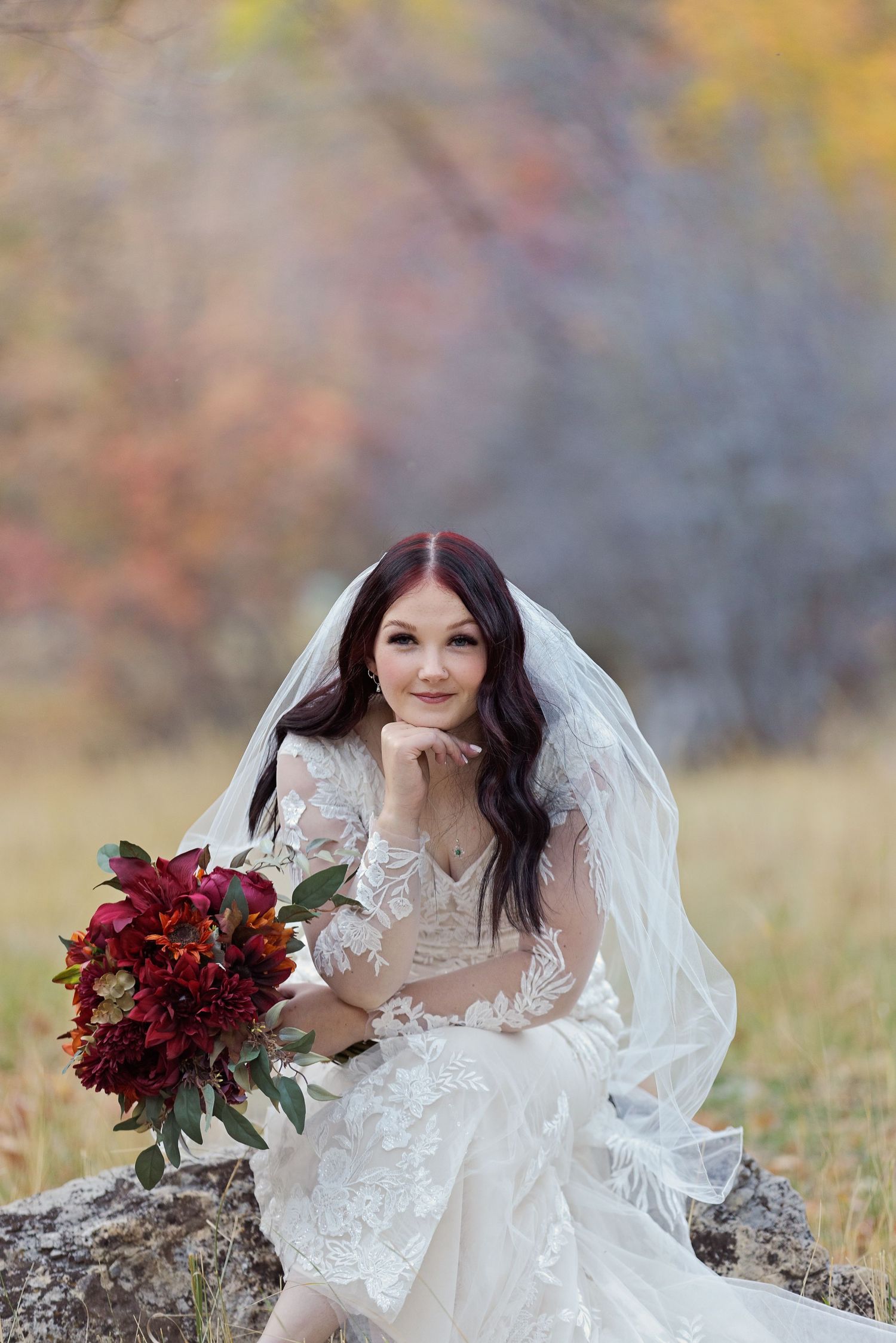 Bridal portrait with burgundy bouquet against autumn foliage background.