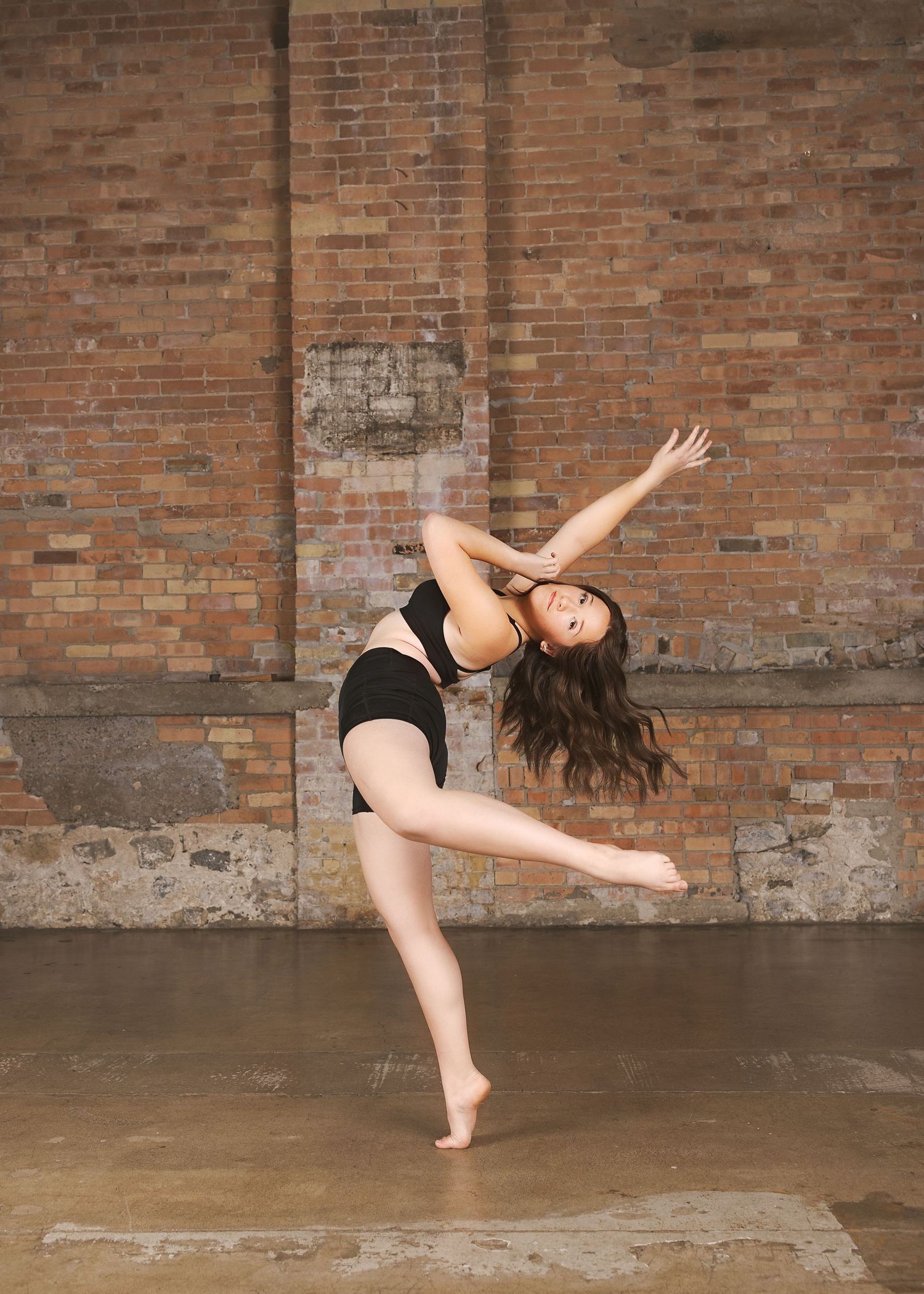 A dancer performs a dynamic contemporary dance sequence against a rustic brick wall backdrop.