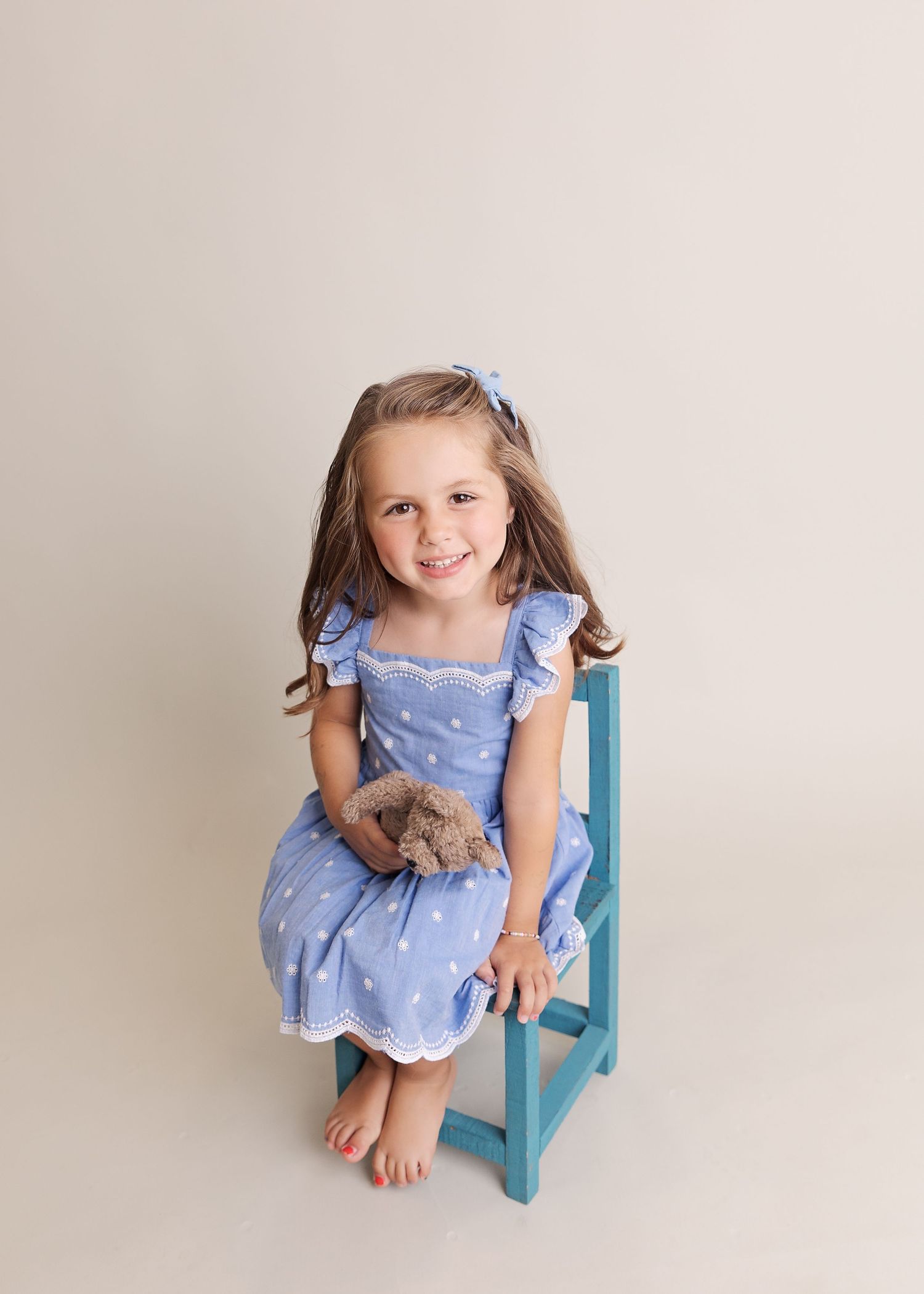 A young child in a polka dot blue dress sitting on a turquoise chair.