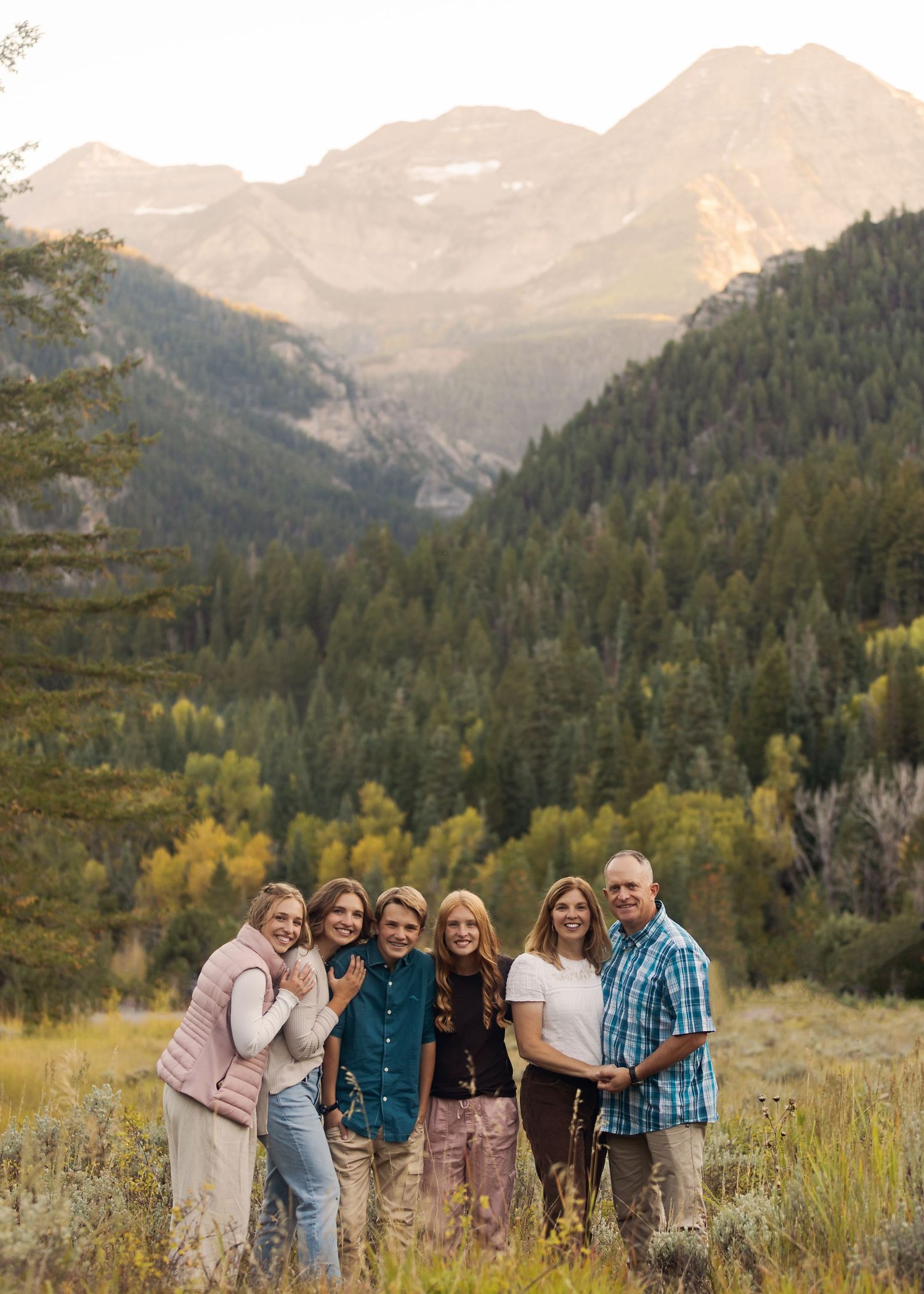 A group poses for a photo in a mountain valley with dramatic peaks and fall foliage in the background.