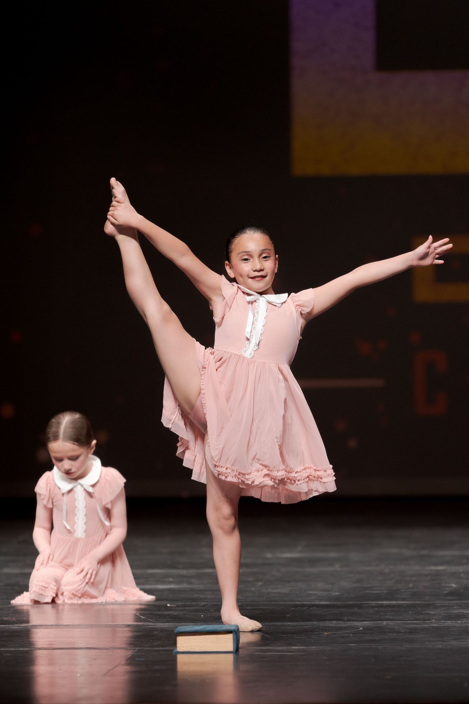 Dancers in pink flowing dresses perform artistic floor movements during a dance recital on stage.