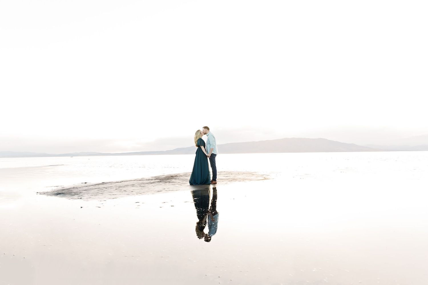 Figure standing on salt flats with reflection in water.