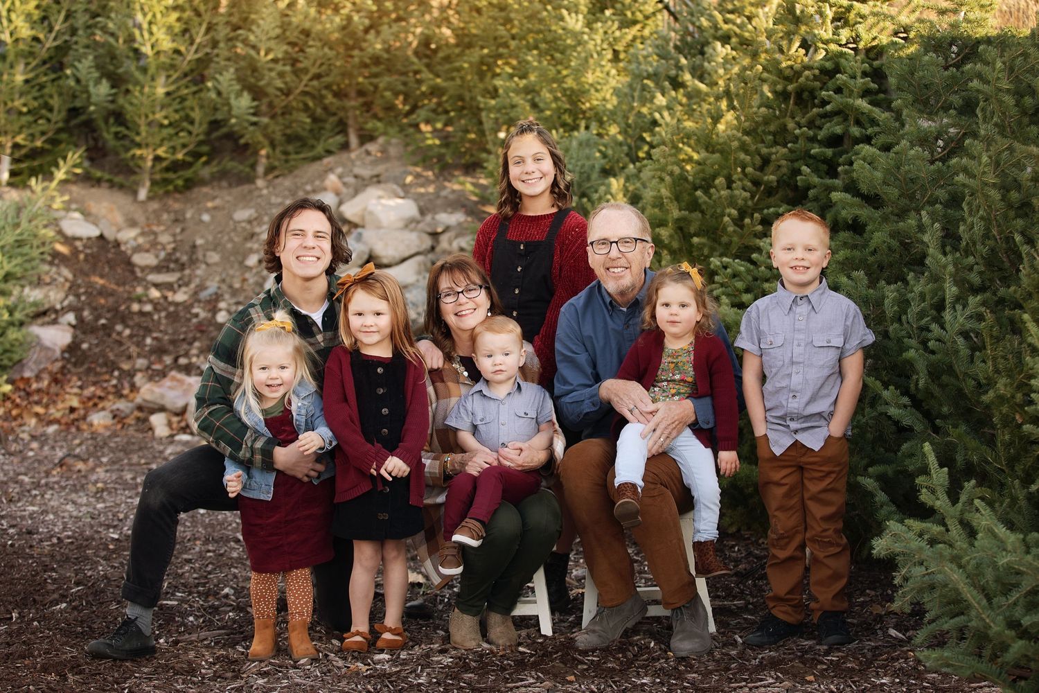 Family portrait outdoors with multiple generations gathered among evergreen trees.