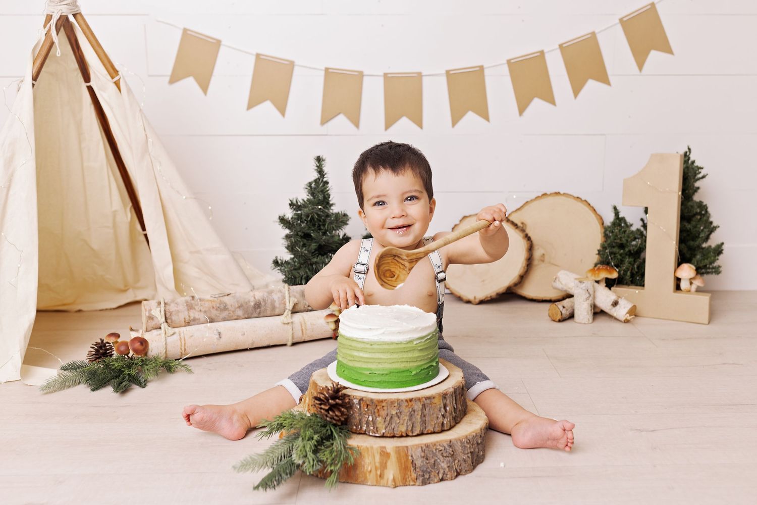 A wooden cake smash photo setup with festive bunting banners and natural rustic decorations against a cream backdrop.