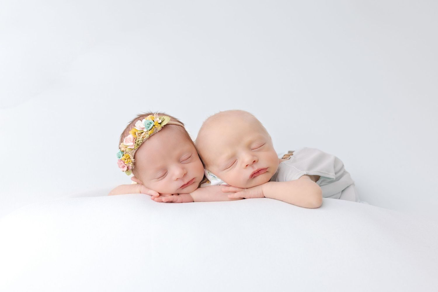 Pair of sleeping newborn babies lying together on white fabric in four different poses.