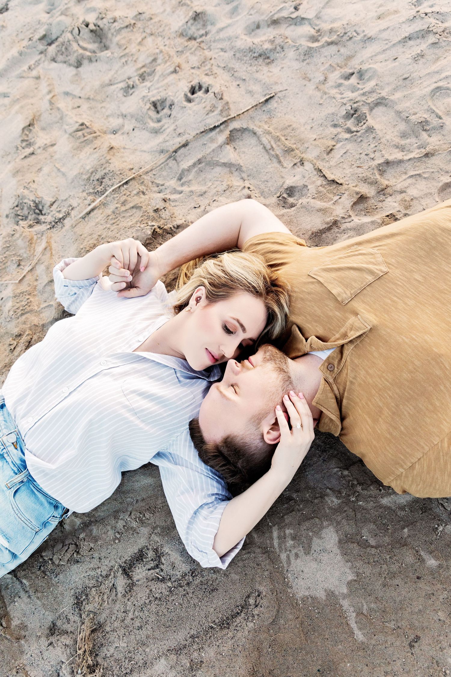 A romantic couple lying together on the beach sand while sharing an intimate moment.