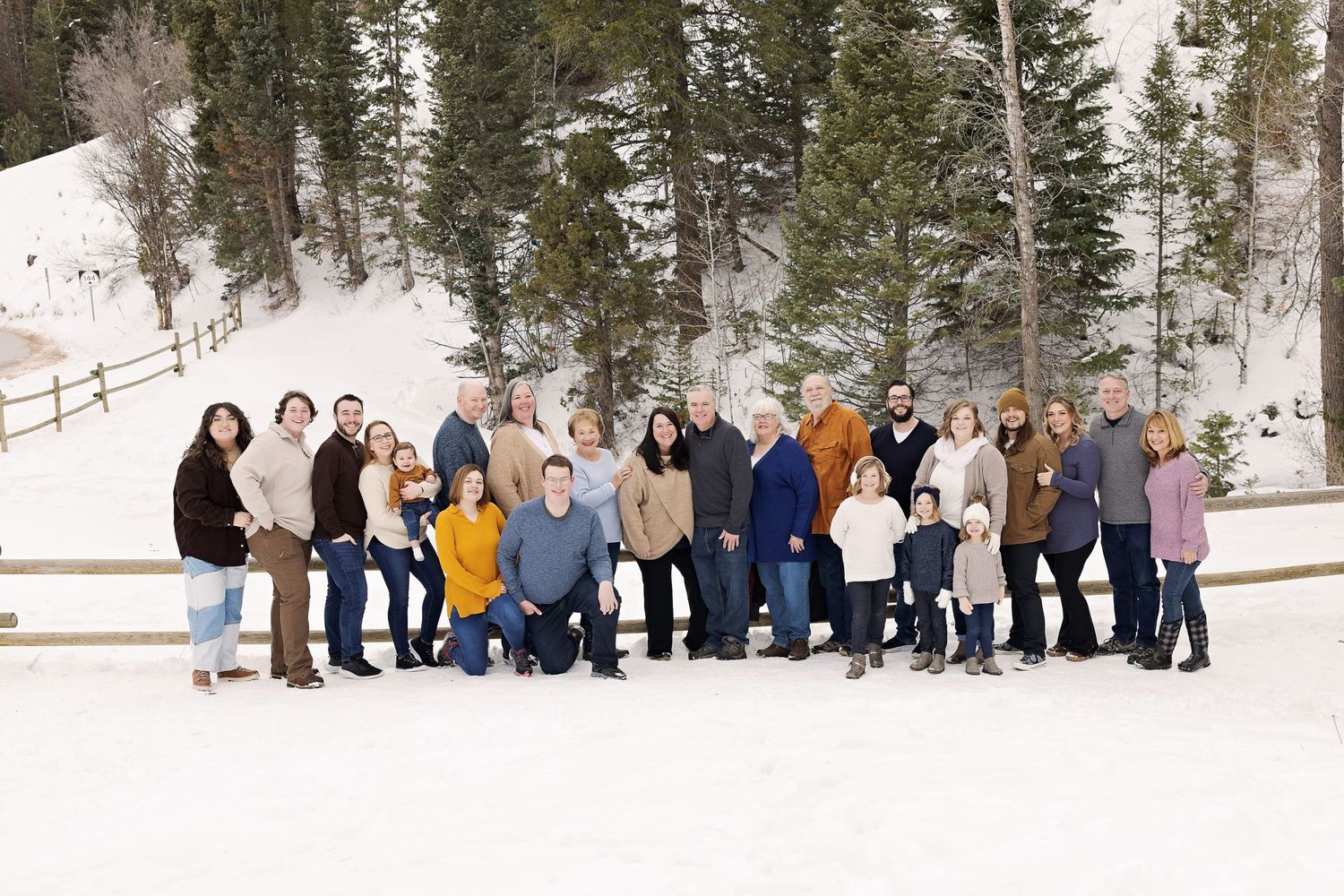 Large extended family group photo in winter scene with snow-covered mountains behind them.