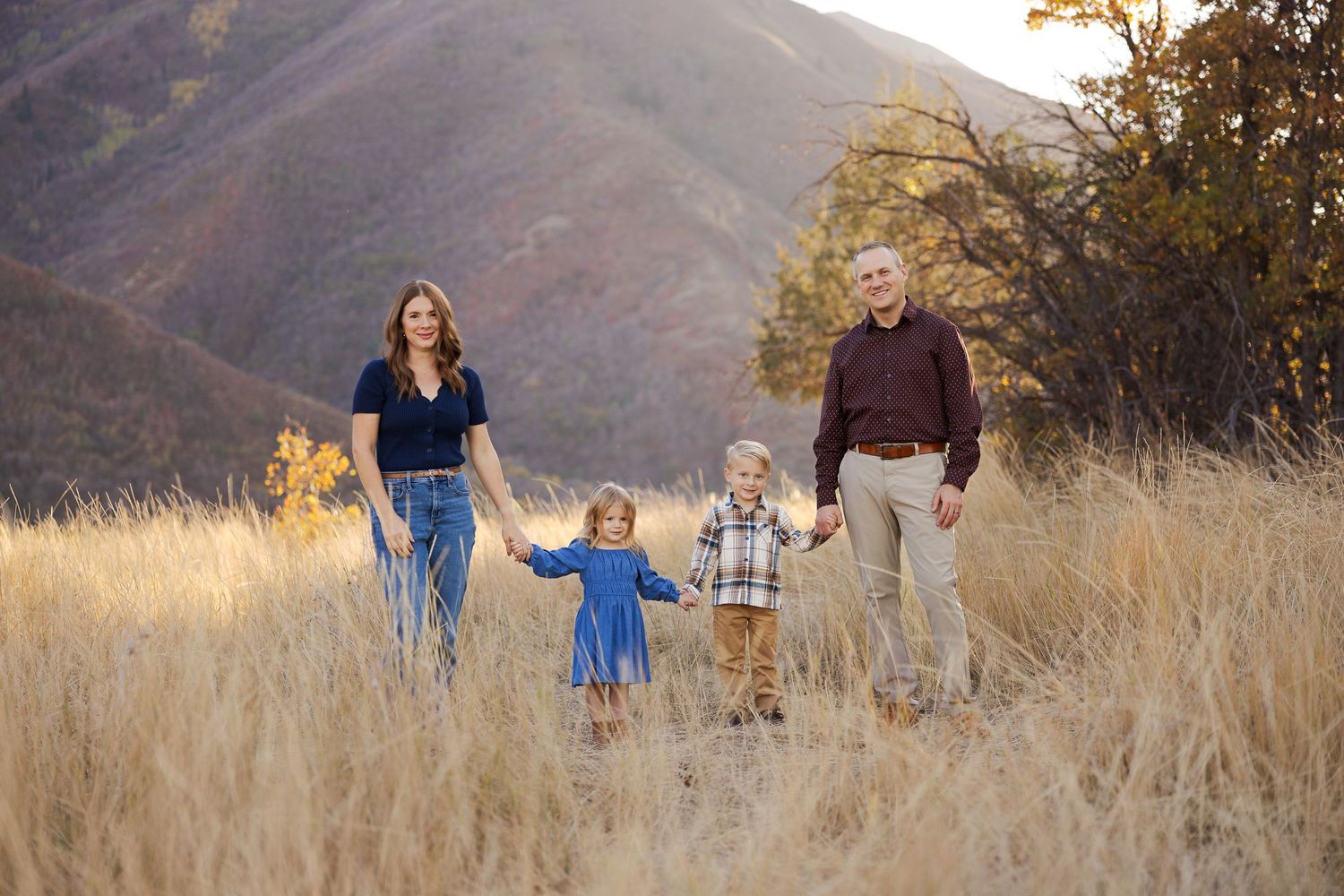 Family walking together in tall golden grass against mountain backdrop.
