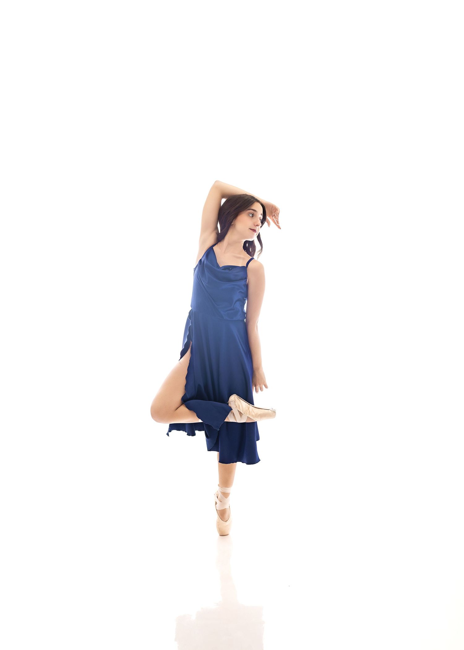 A ballet dancer in a navy dress performs a graceful pose en pointe against a white background.