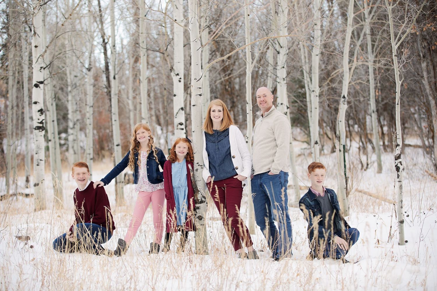 Family group poses together in a snowy aspen forest wearing coordinated winter outfits.