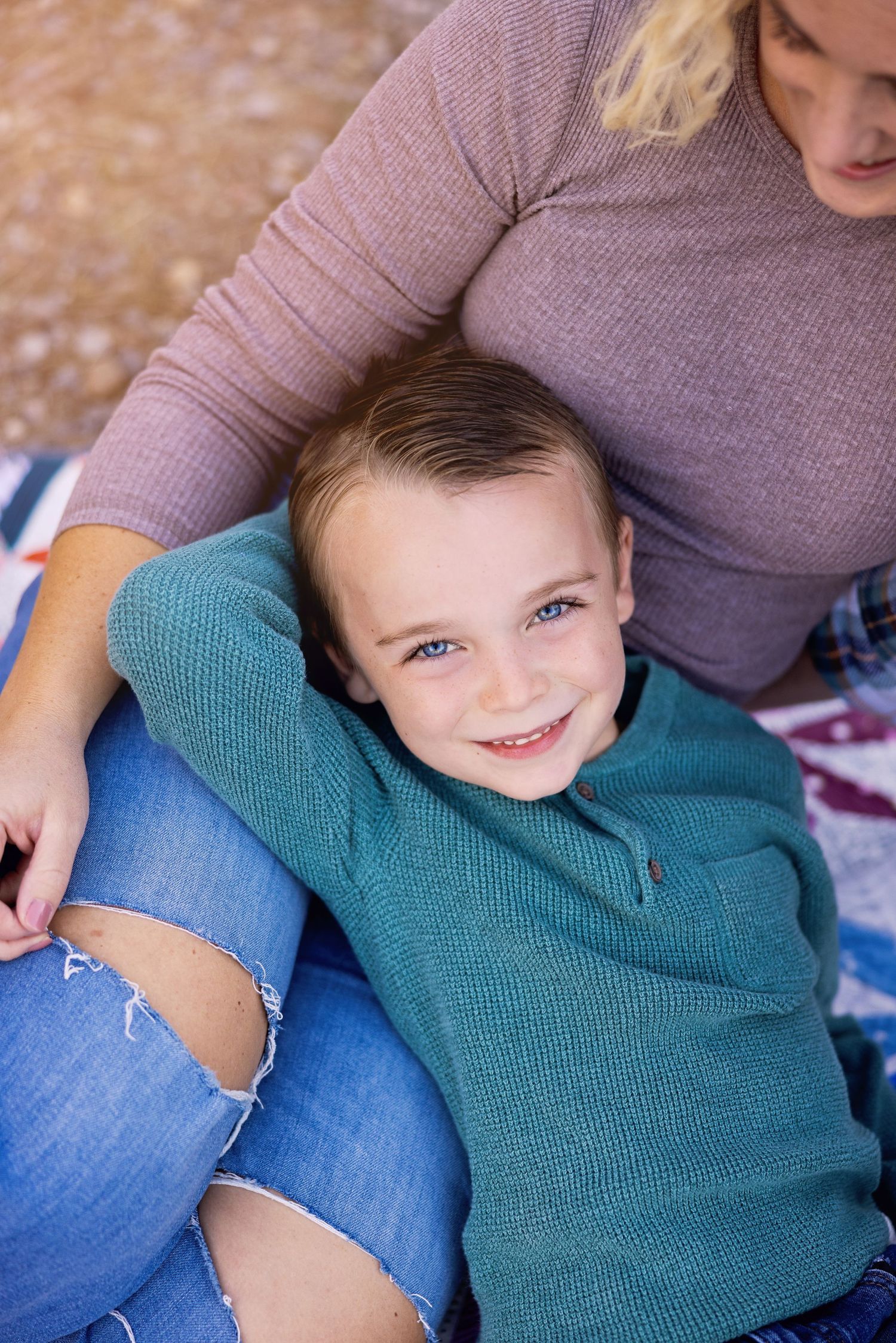 Casual portrait of person in teal sweater resting on lap in ripped jeans.