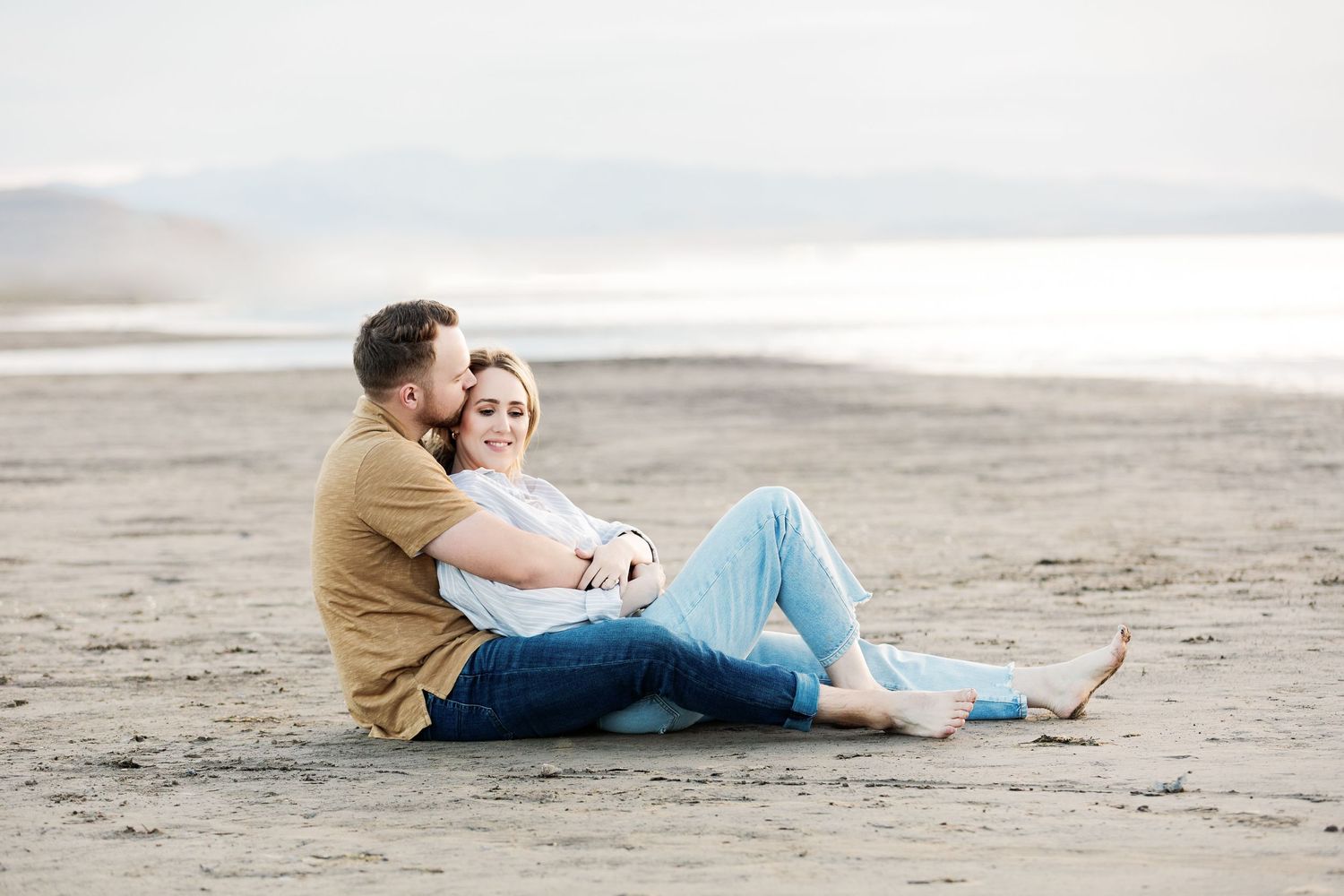 A couple relaxes together on a misty beach at sunset.