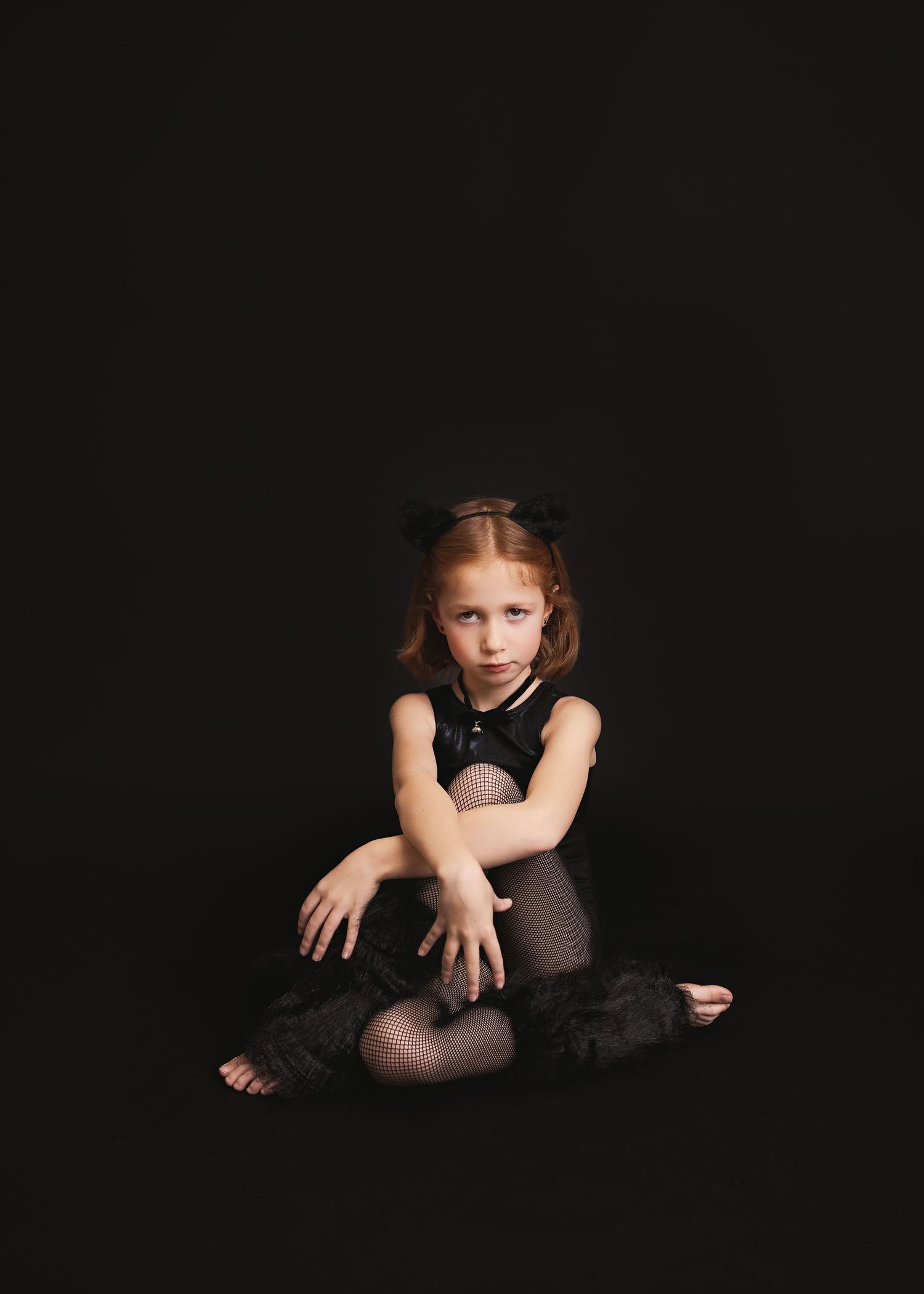 Young dancer in black leotard and tights sits on dark floor in dramatic lighting during dance performance.