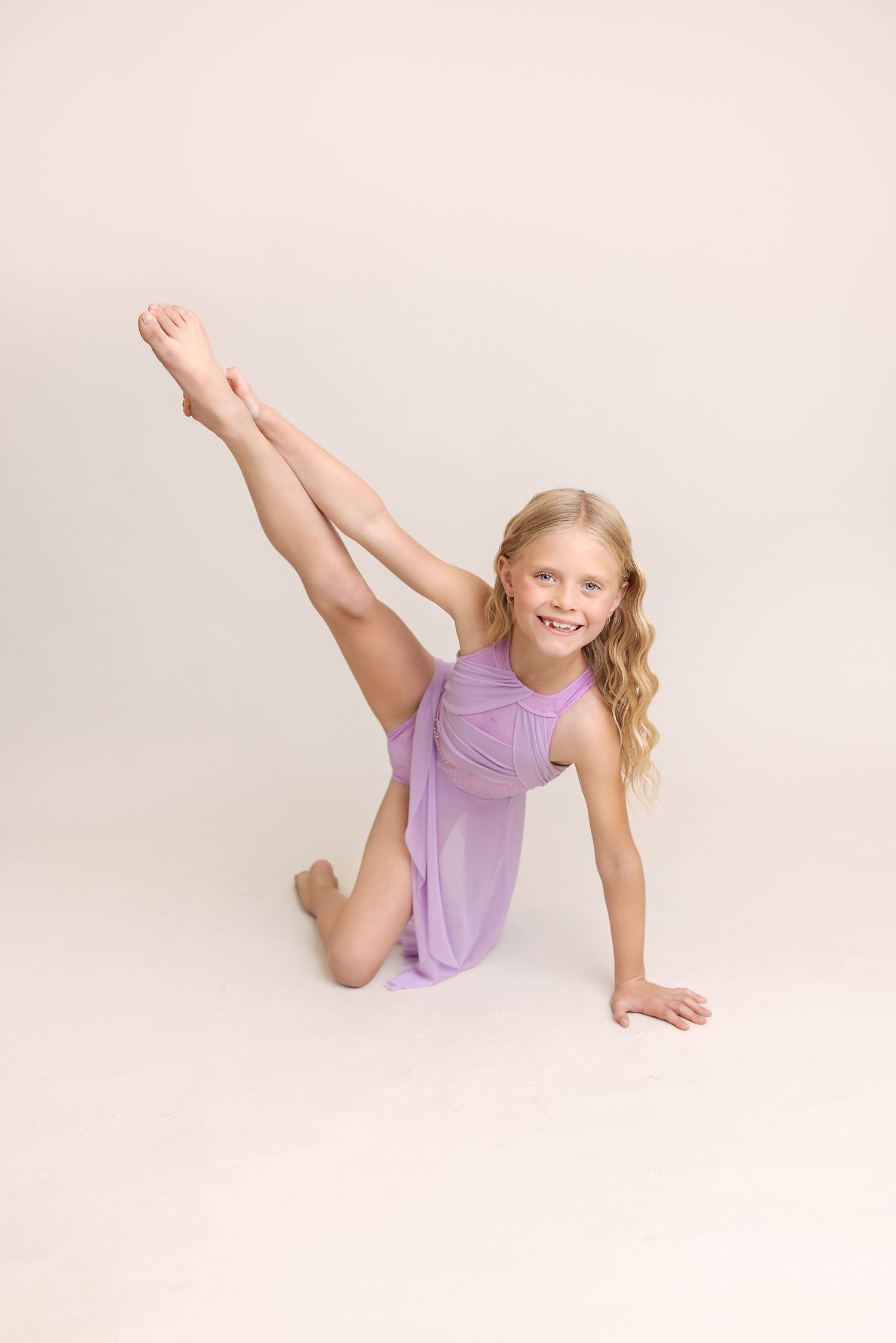 Young dancer in purple leotard performs split pose during studio photoshoot.