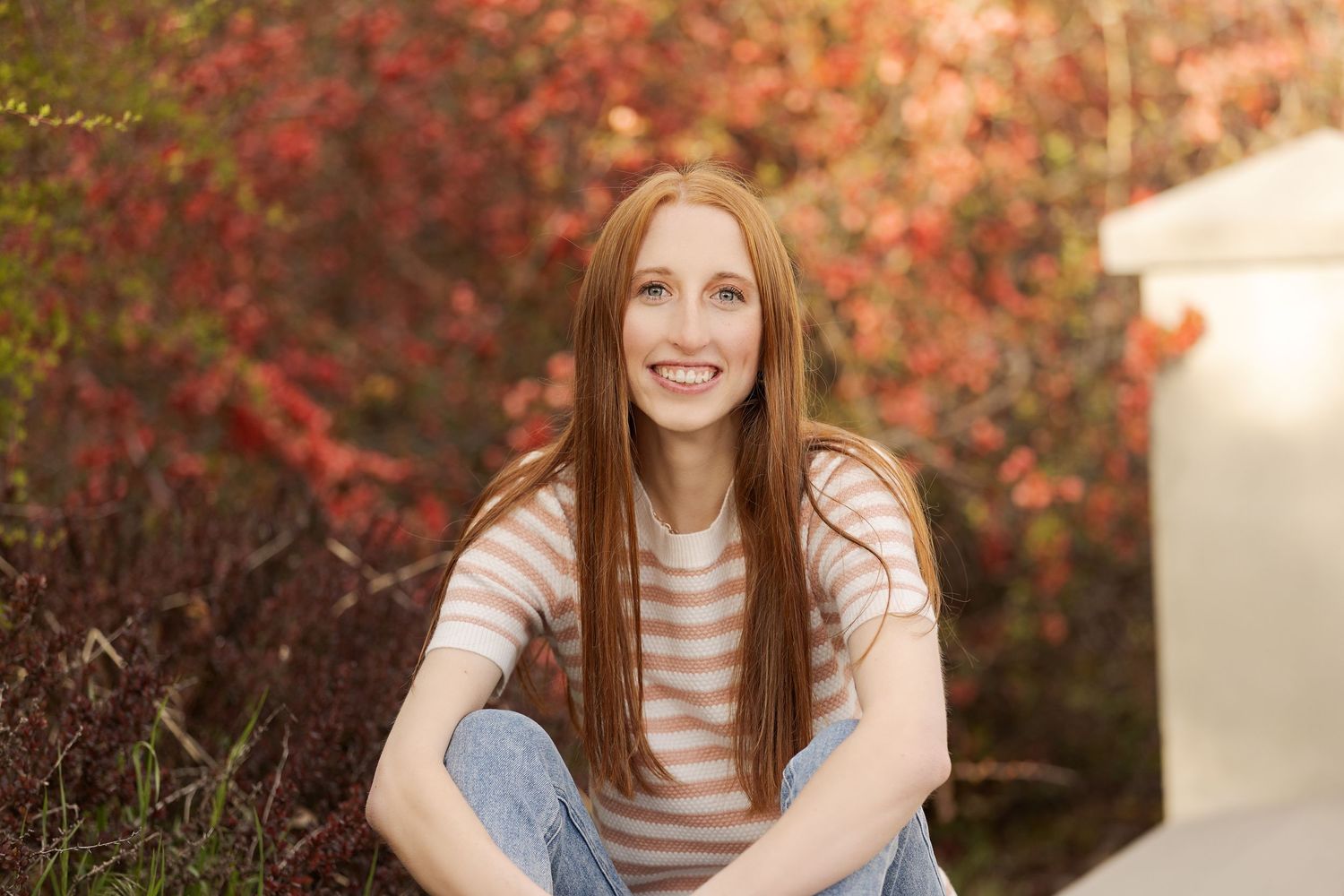 Casual outdoor portrait with red autumn foliage in background.