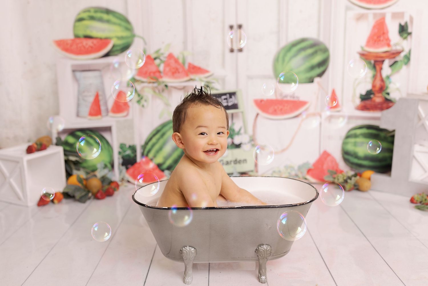 A rustic white backdrop with summer watermelon themes and props creates a colorful and festive photoshoot setting.