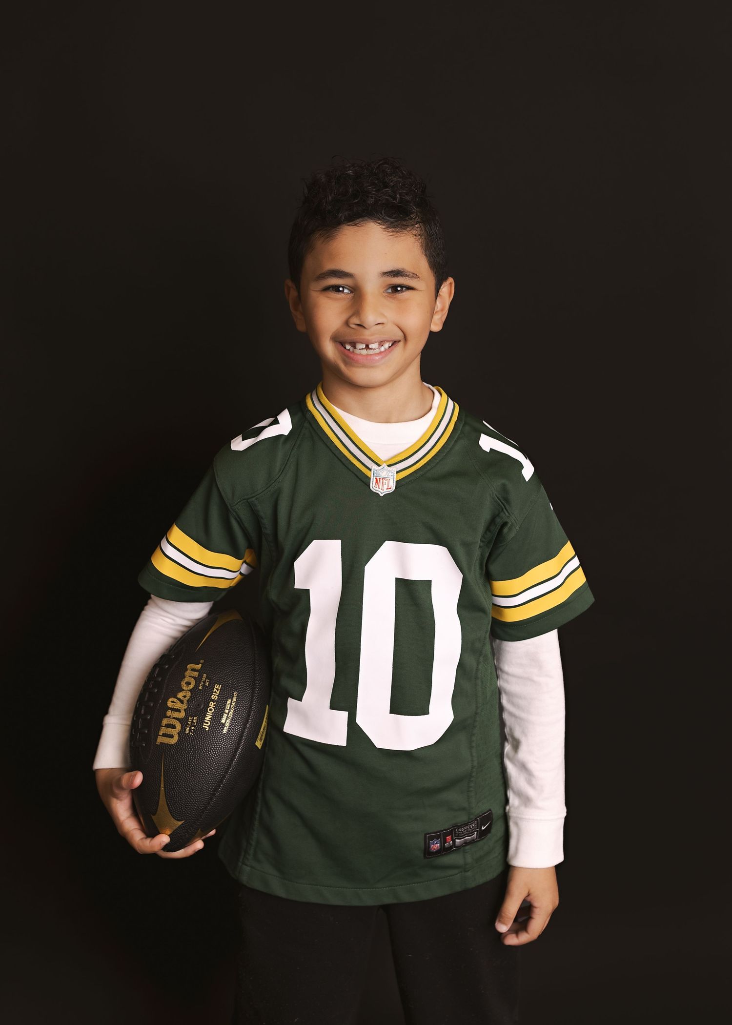 Four photos of a young sports fan wearing different Green Bay Packers jerseys while holding a football against a dark background.