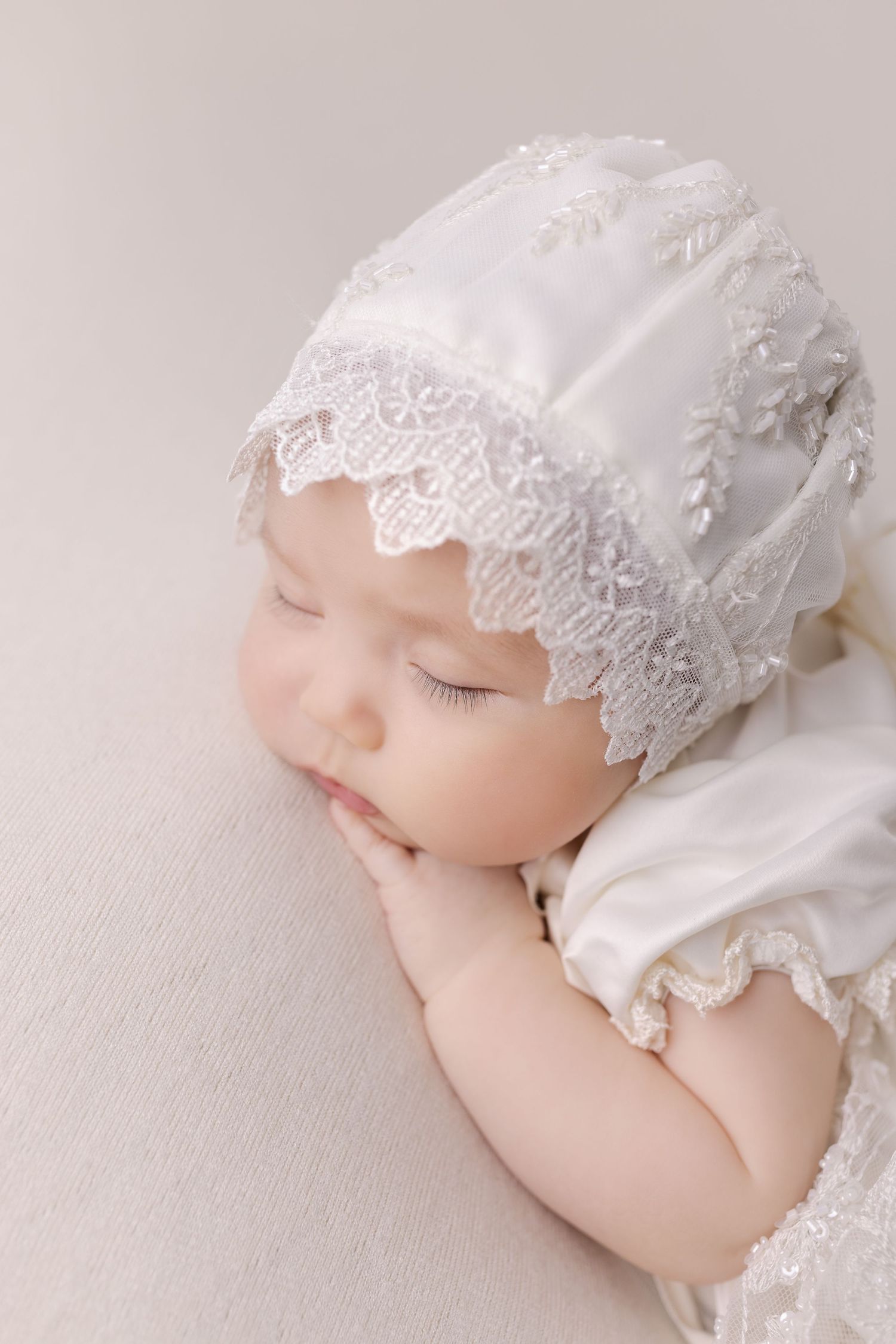 Sleeping baby in white lace bonnet and christening dress.