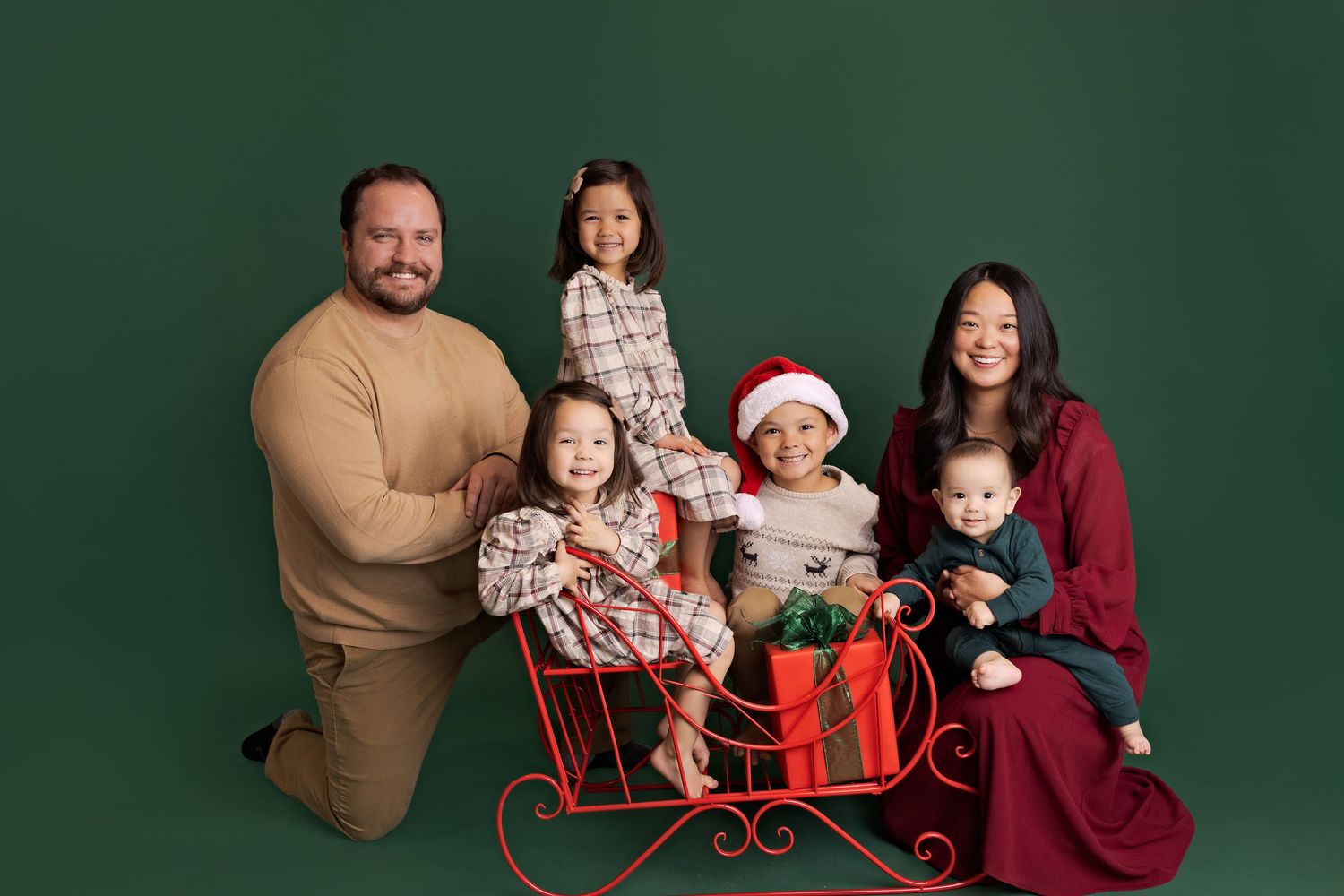 A group poses in coordinated holiday outfits against a dark green backdrop for a festive Christmas portrait session.
