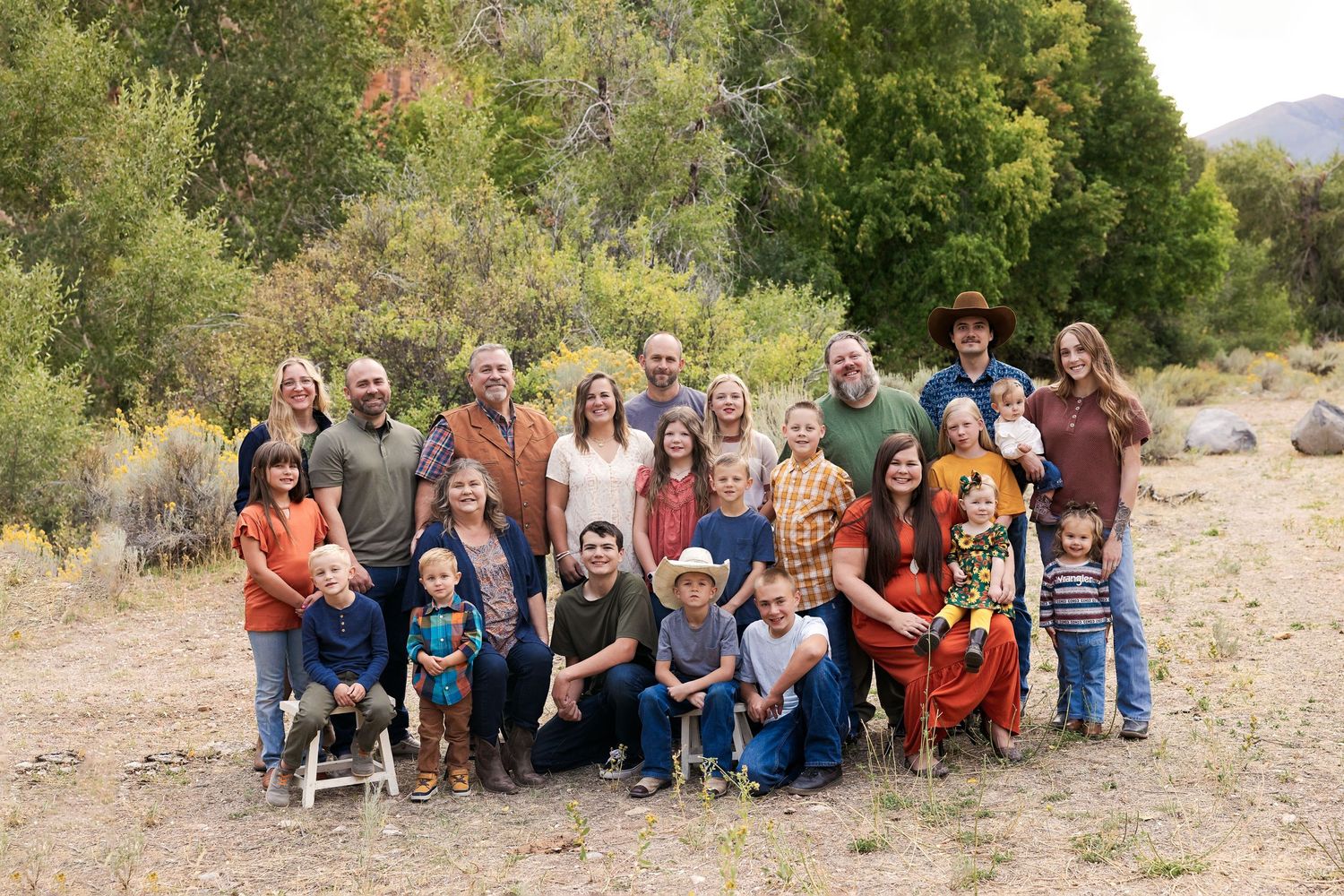 Large multigenerational family portrait outdoors in autumn, posing together in a natural setting with colorful fall foliage.