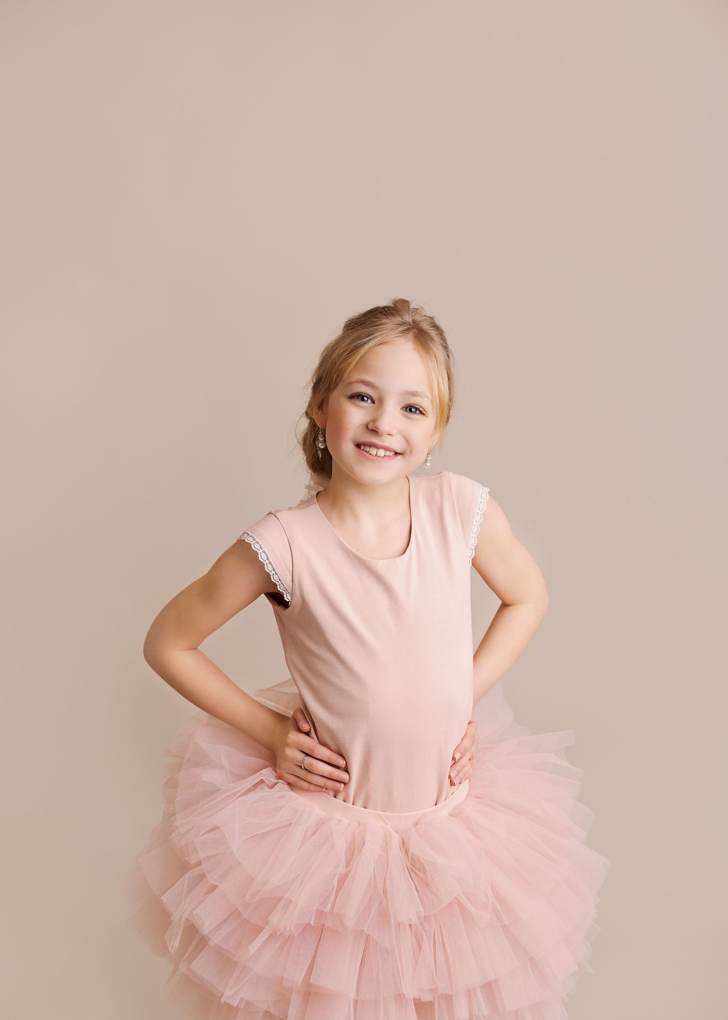 Cheerful young dancer striking pose in layered pink tutu against neutral background.