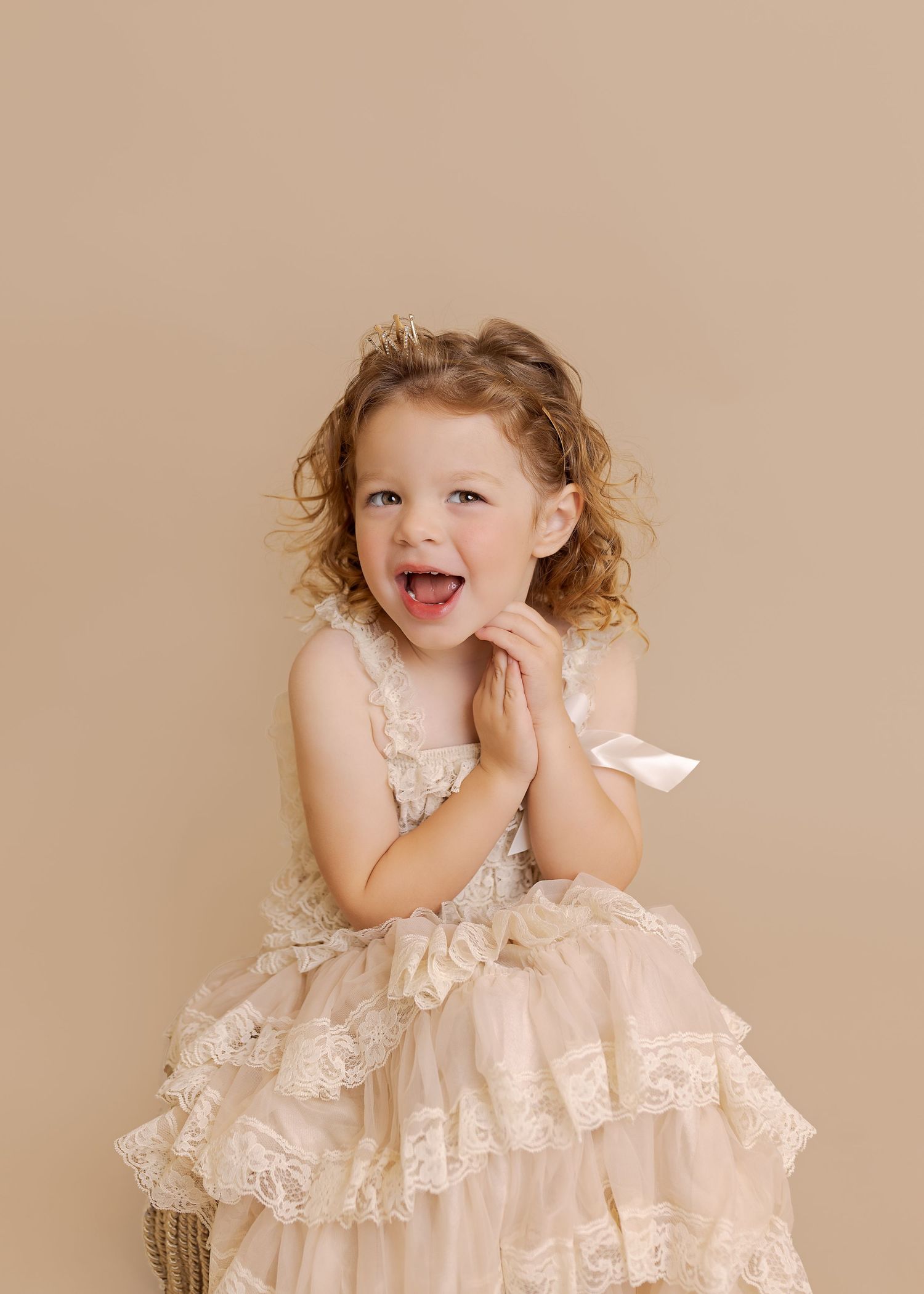 A delicate pink lace dress with ruffled layers and bows photographed against a beige background.
