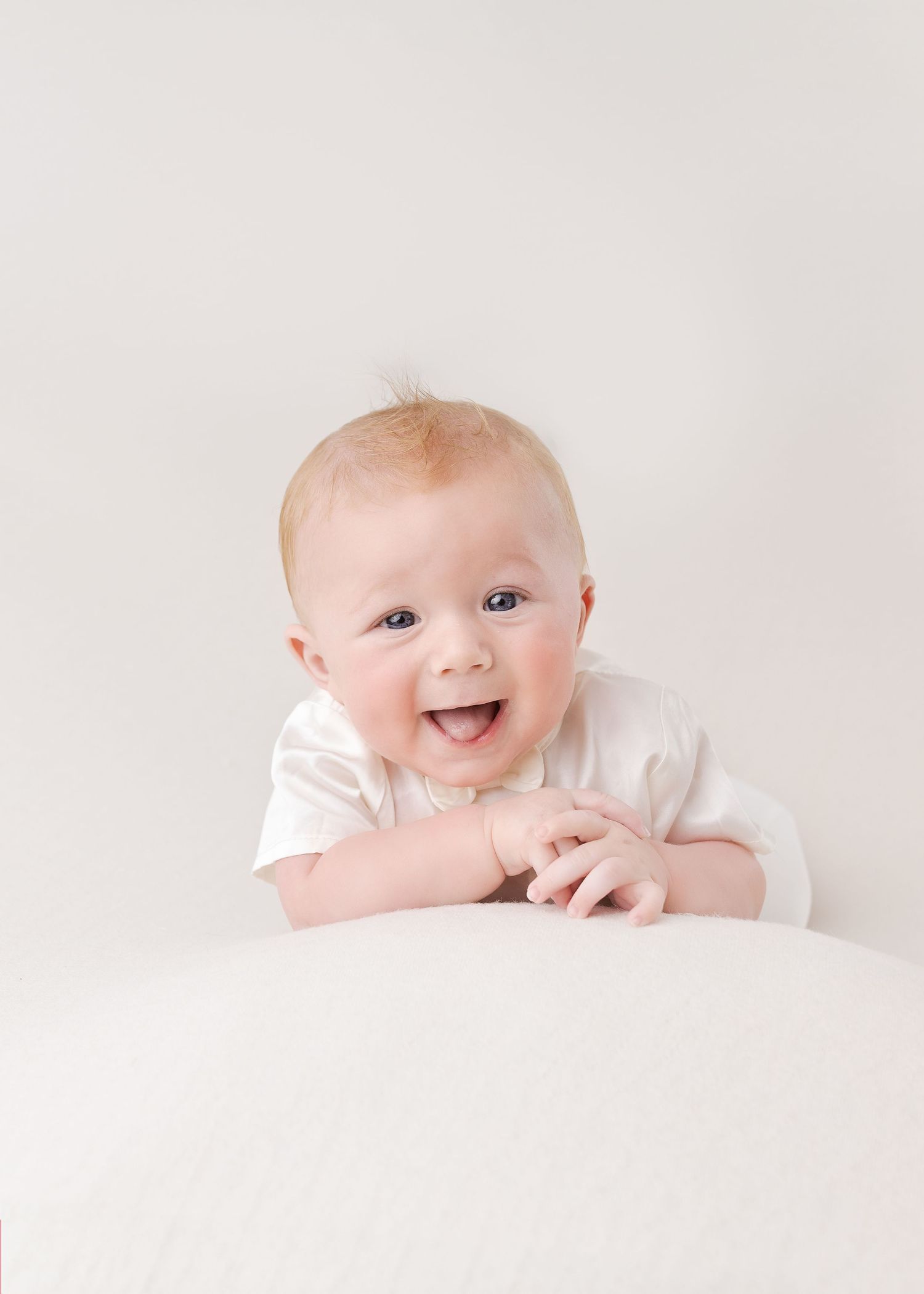 Happy baby in white outfit laying on light background with joyful smile.